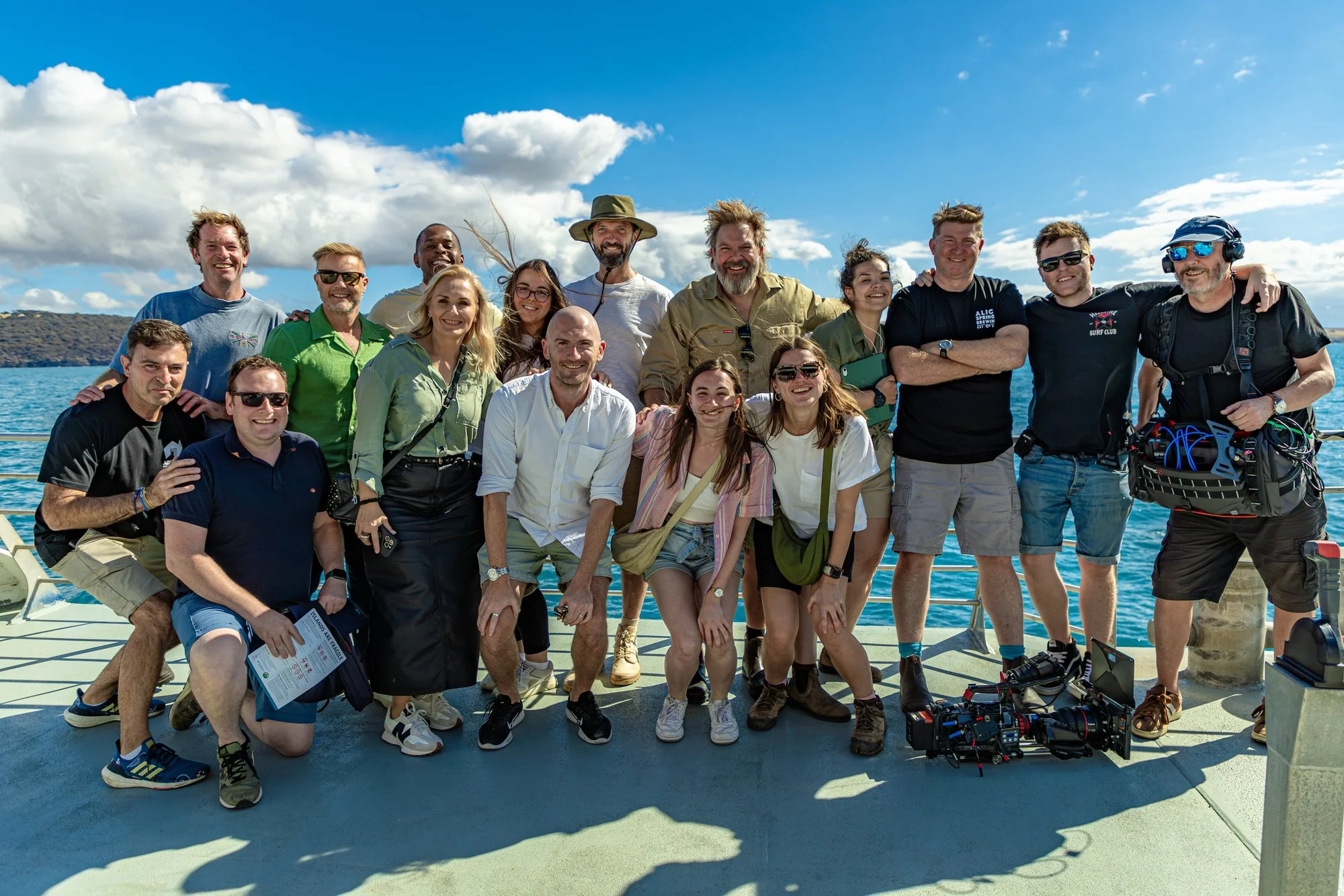 Group of people smiling and posing for a photo on a boat with water and blue sky in the background.