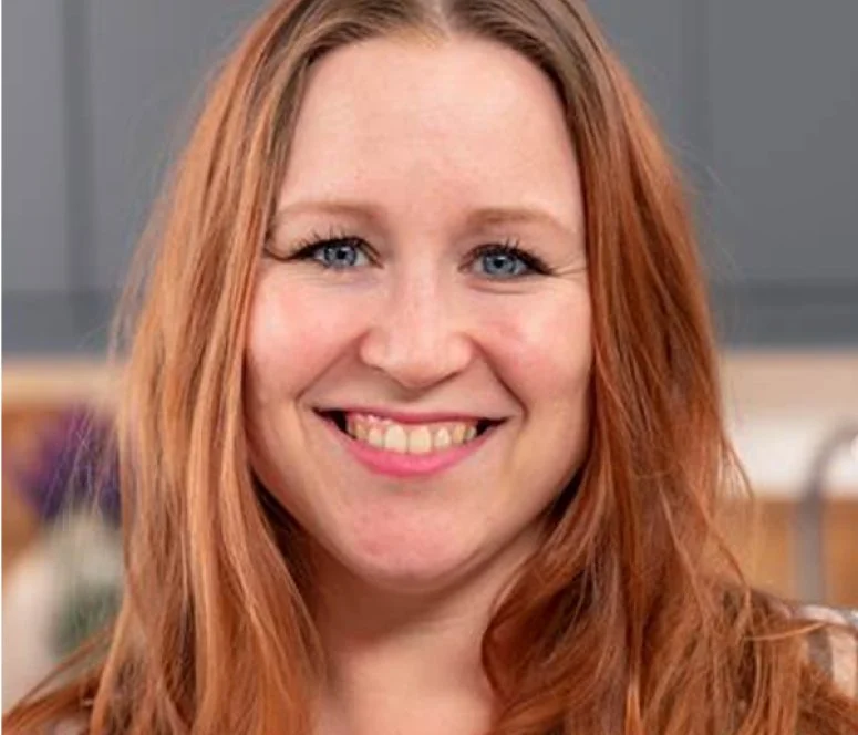 A woman with long red hair and blue eyes smiling.