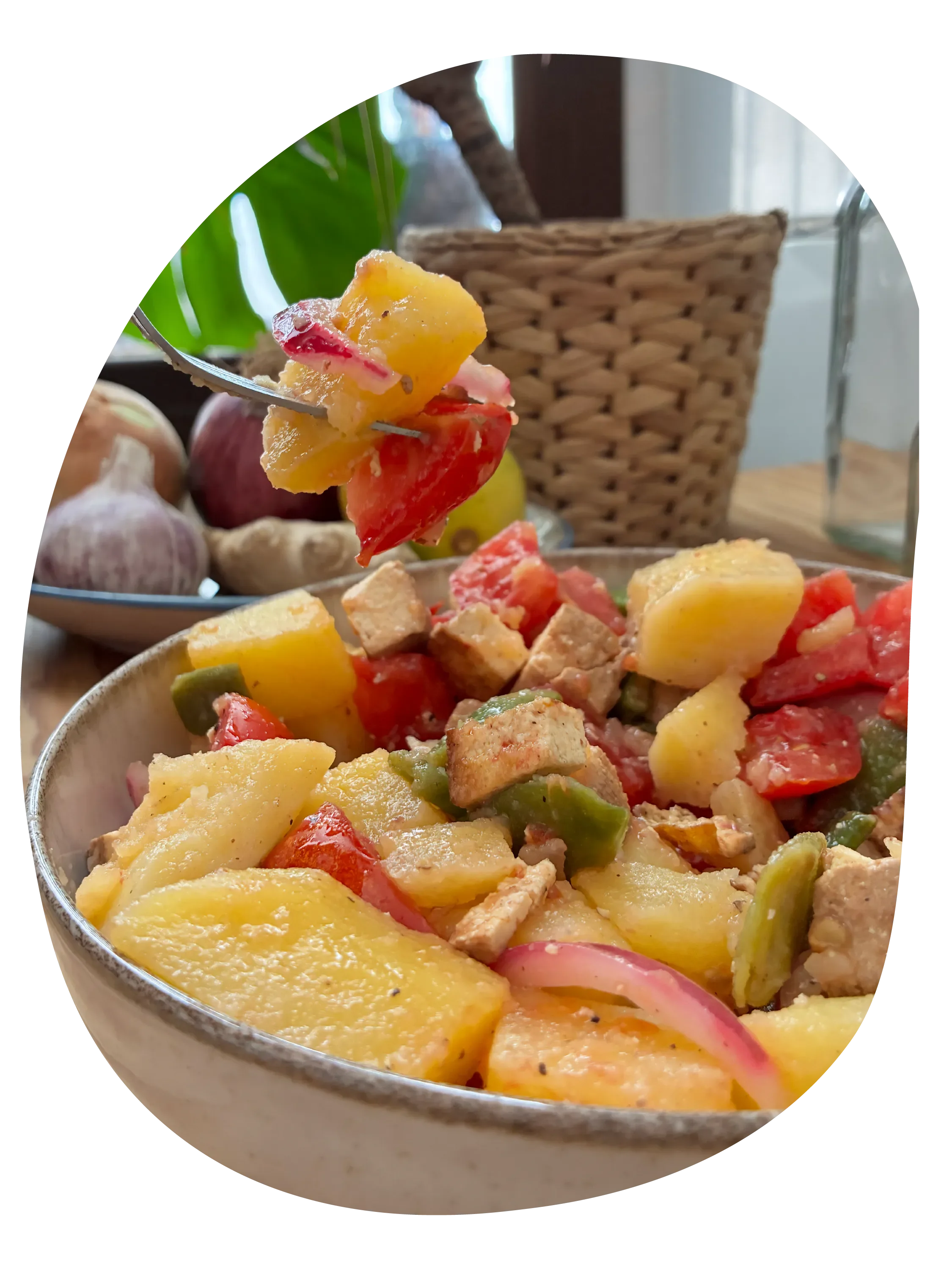 Ensalada fría de patatas cocidas con tomates, judías planas, tofu ahumado y cebolla morada encurtida, acompañada con un plato de frutas en el fondo.