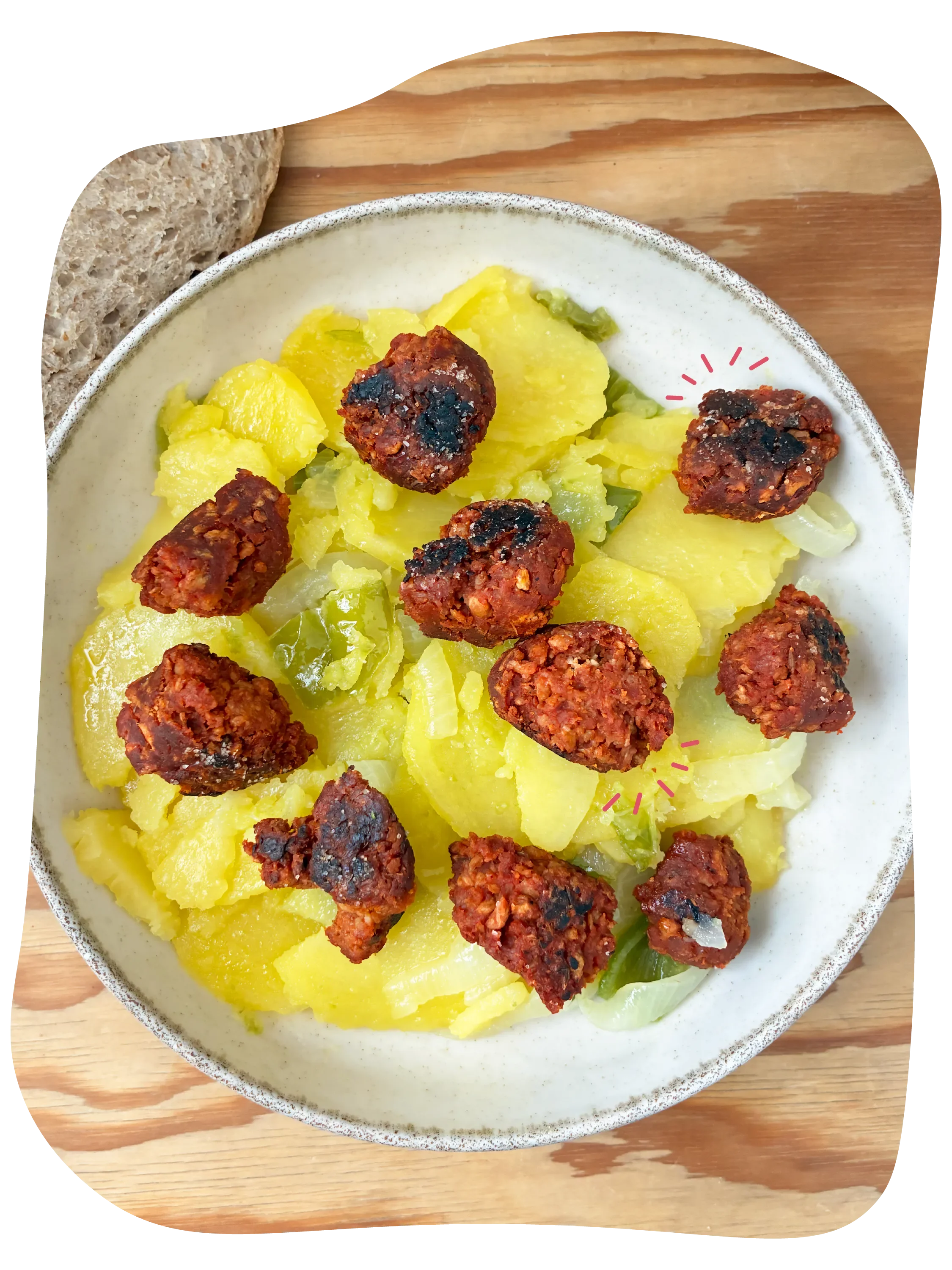 Plato con albóndigas de carne, papas cocidas, cebolla y guisantes en un plato blanco sobre una tabla de madera.