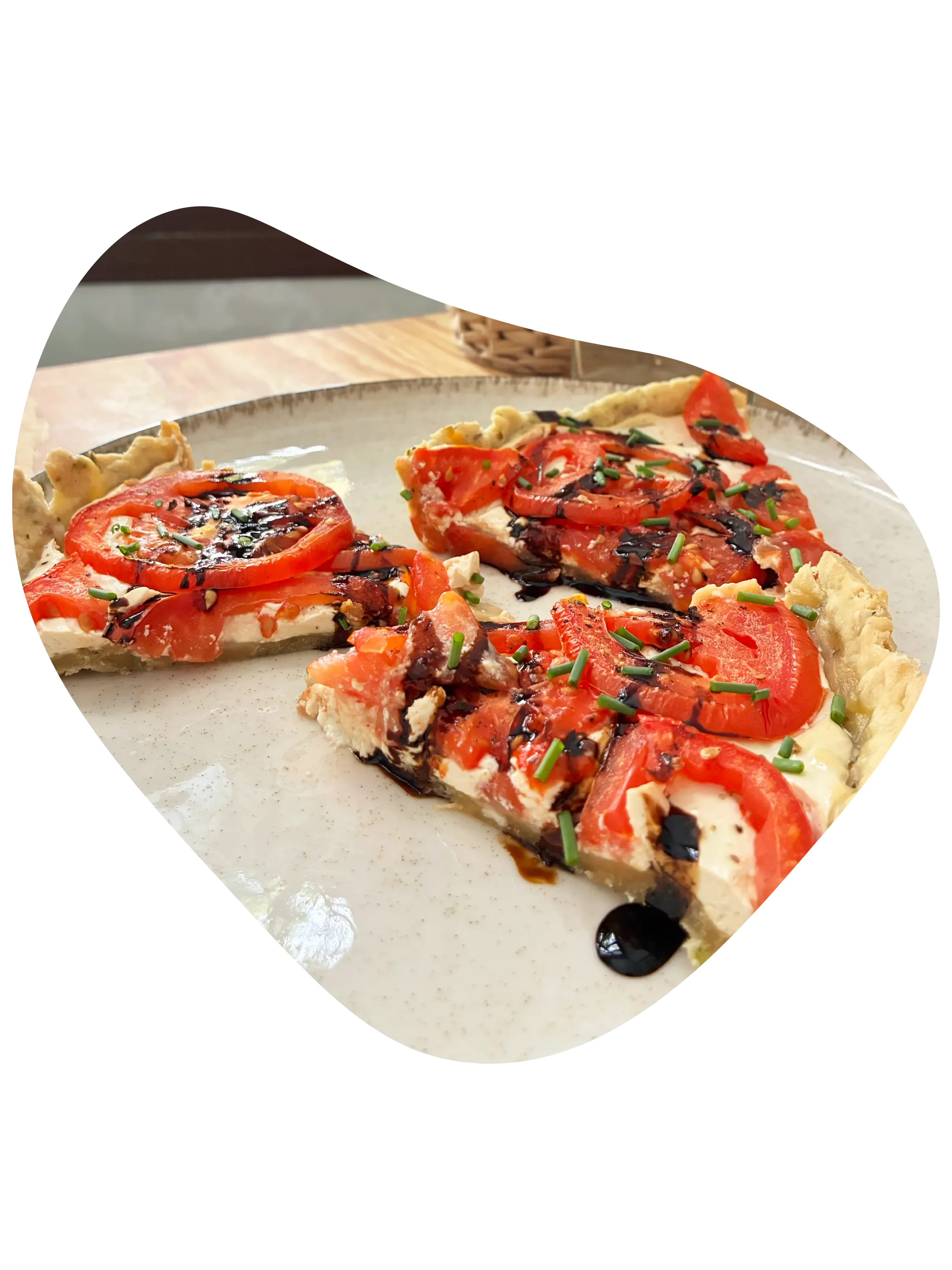Porción de hojaldre con tomate, queso, crema de vinagre de Módena y cebollino en plato de cerámica blanco.