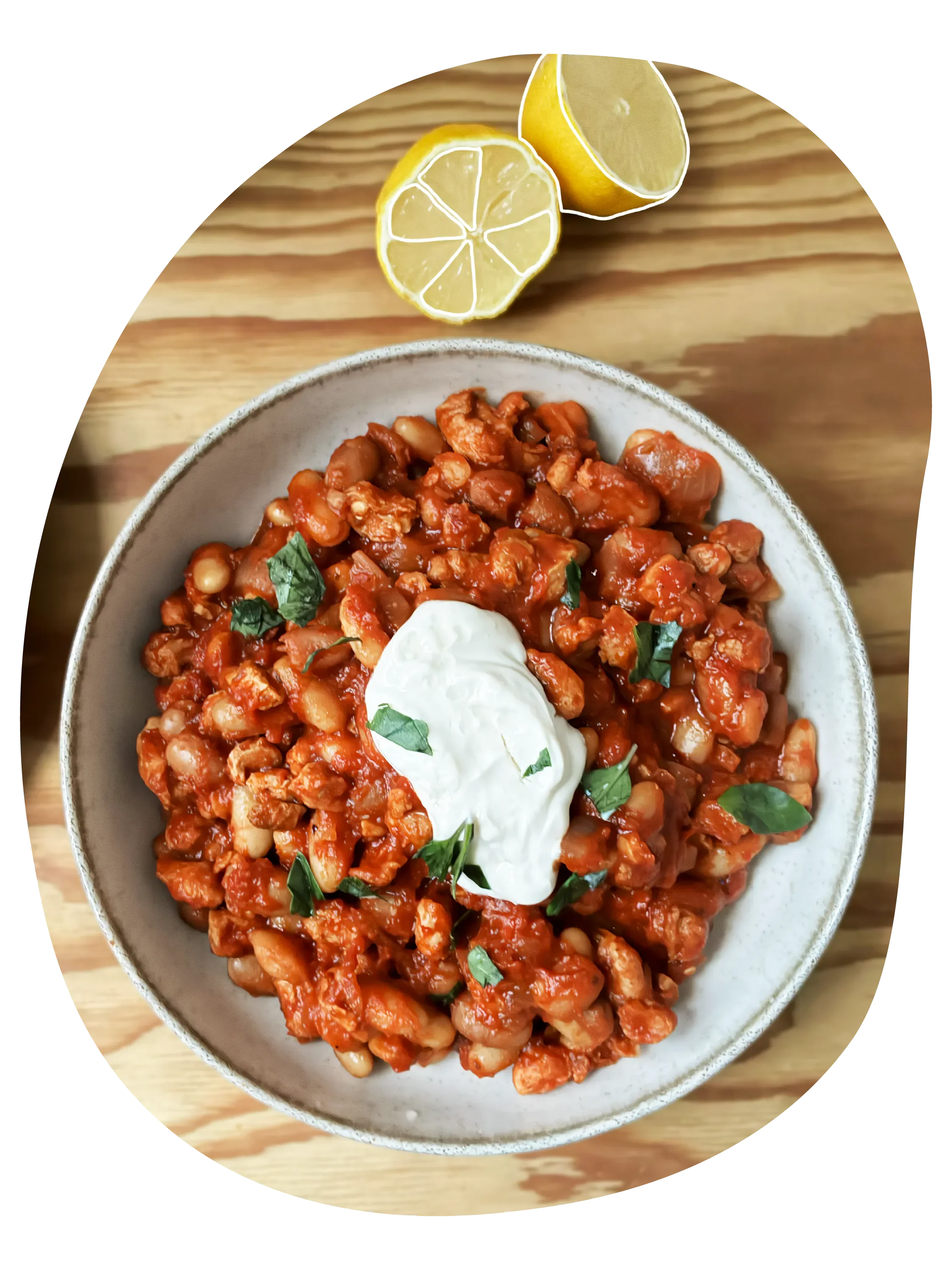 Plato de chili vegano con soja texturizada y frijoles, con crema de queso vegano encima y hojas de cilantro, acompañado de medio limón sobre una superficie de madera.