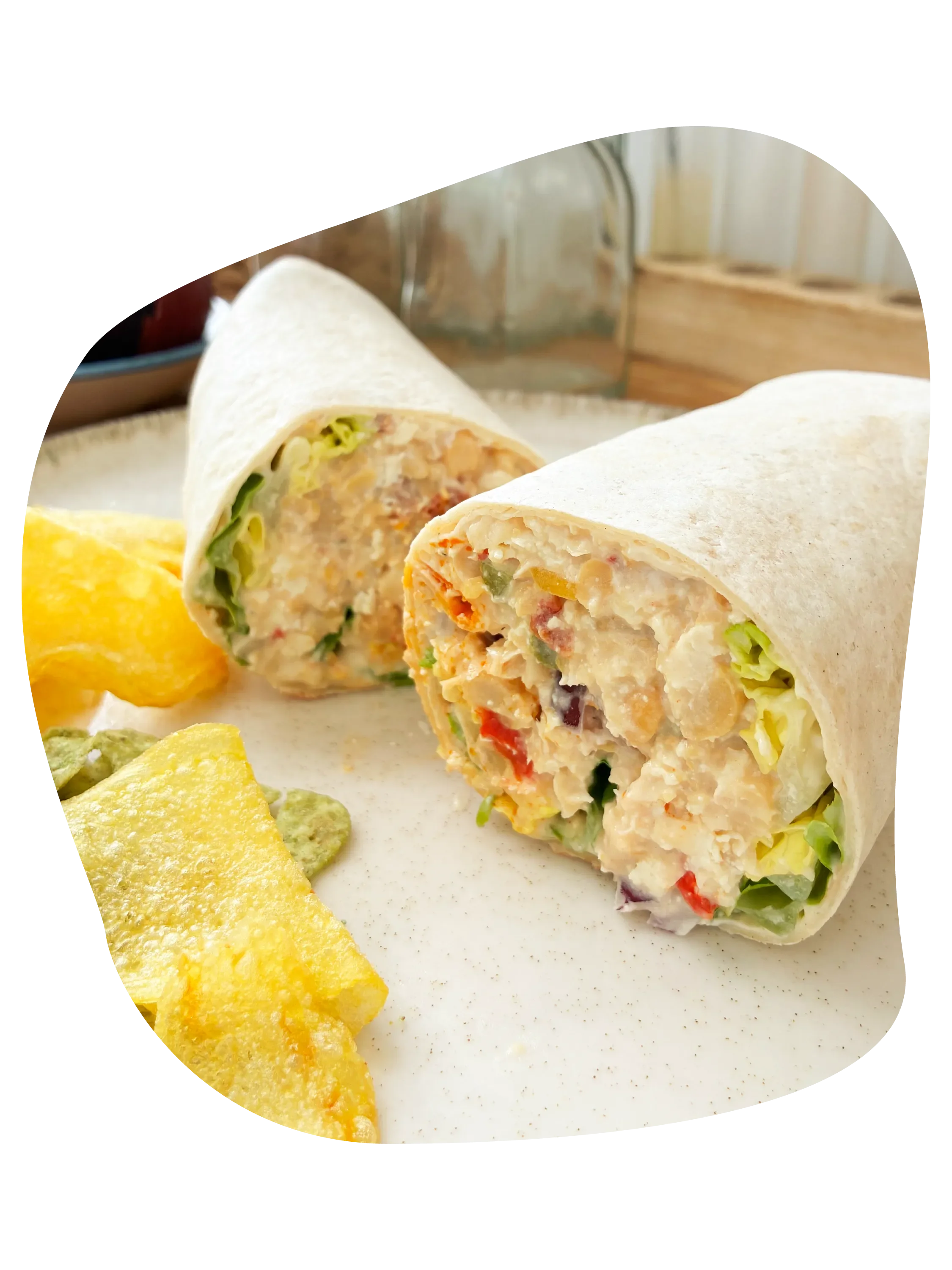 Wrap con tortilla de harina y avena partido por la mitad con ingredientes como garbanzos, lechuga, tomate y cebolla, acompañado de nachos de maíz y guacamole