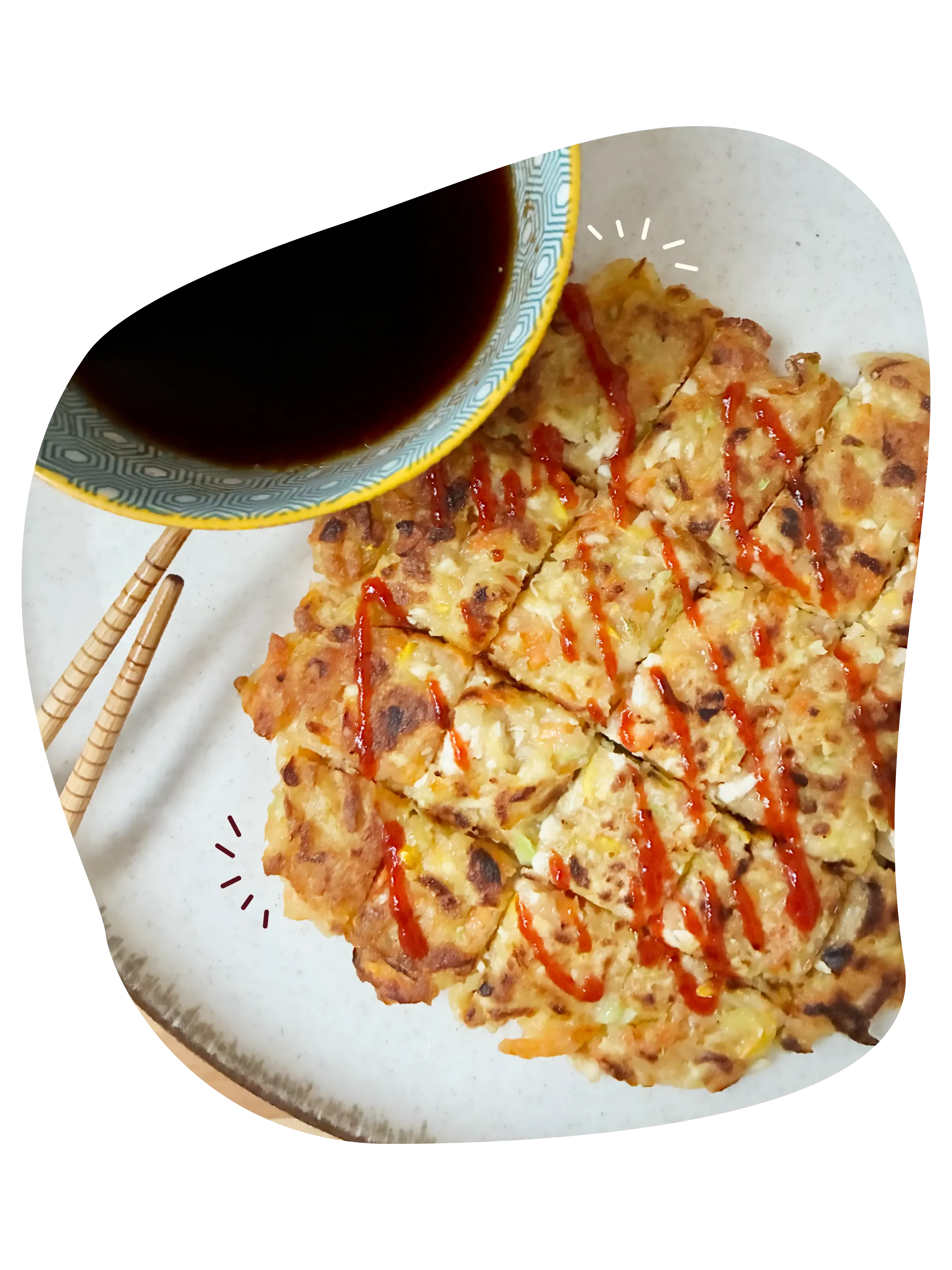 Yachaejeon de verduras con salsa sriracha por encima, palillos de madera y un bol con salsa de soja para acompañar.