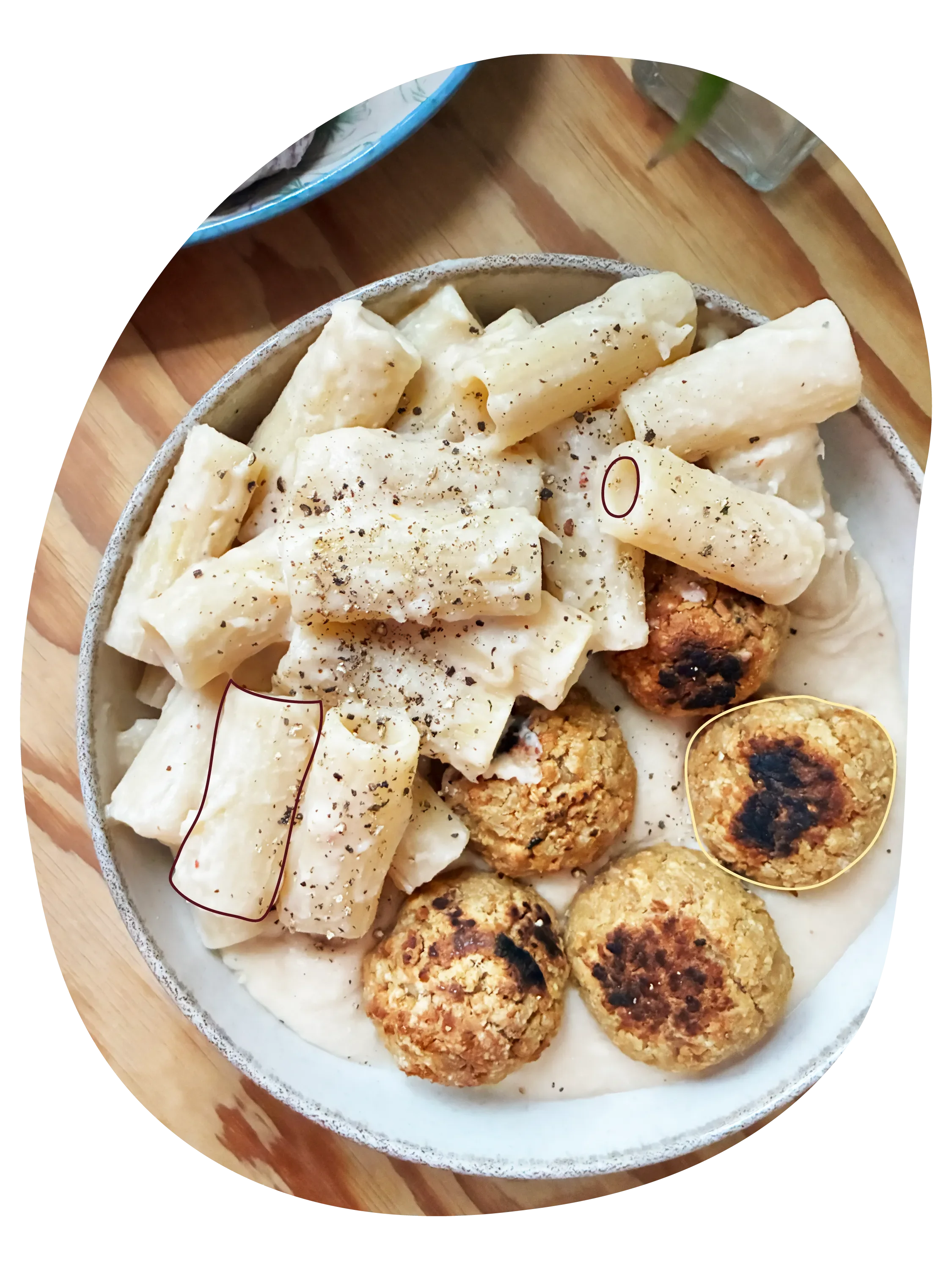 Plato de pasta cremosa con salsa de alubias y albóndigas veganas, sobre una mesa de madera.