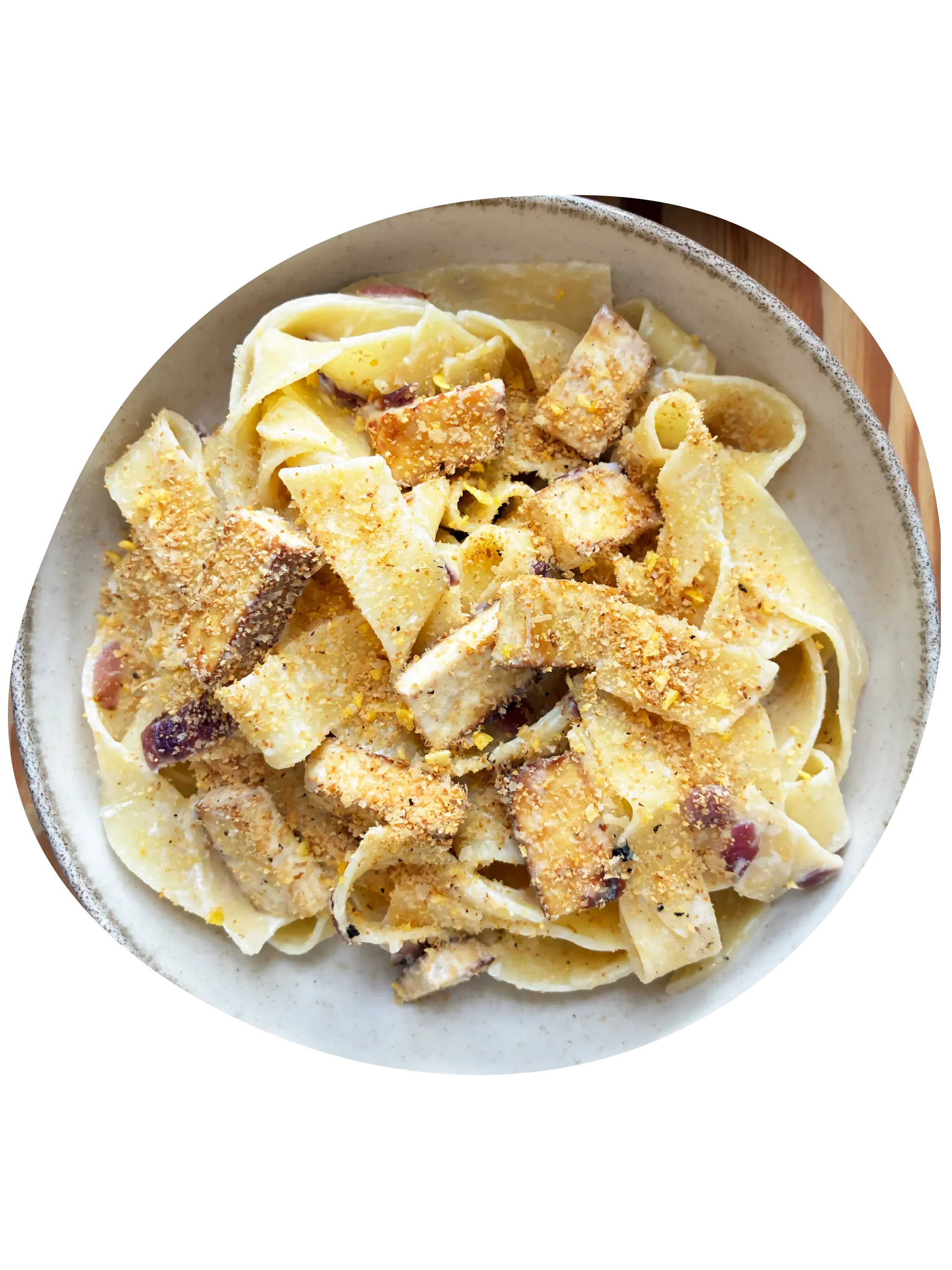 Pasta estilo pappardelle alla carbonara vegana con tofu ahumado, cebolla morada y salsa de queso crema, servido en un plato blanco.
