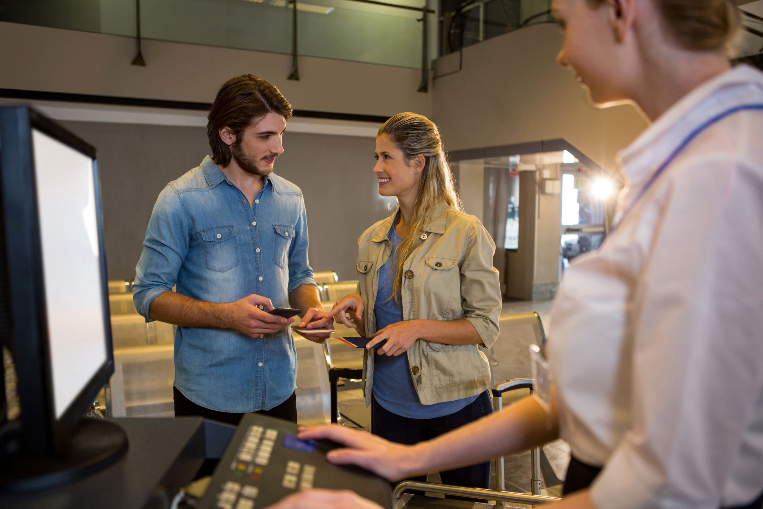 A man and woman engaged in conversation at an airport check-in counter, with a woman in the foreground using a computer.