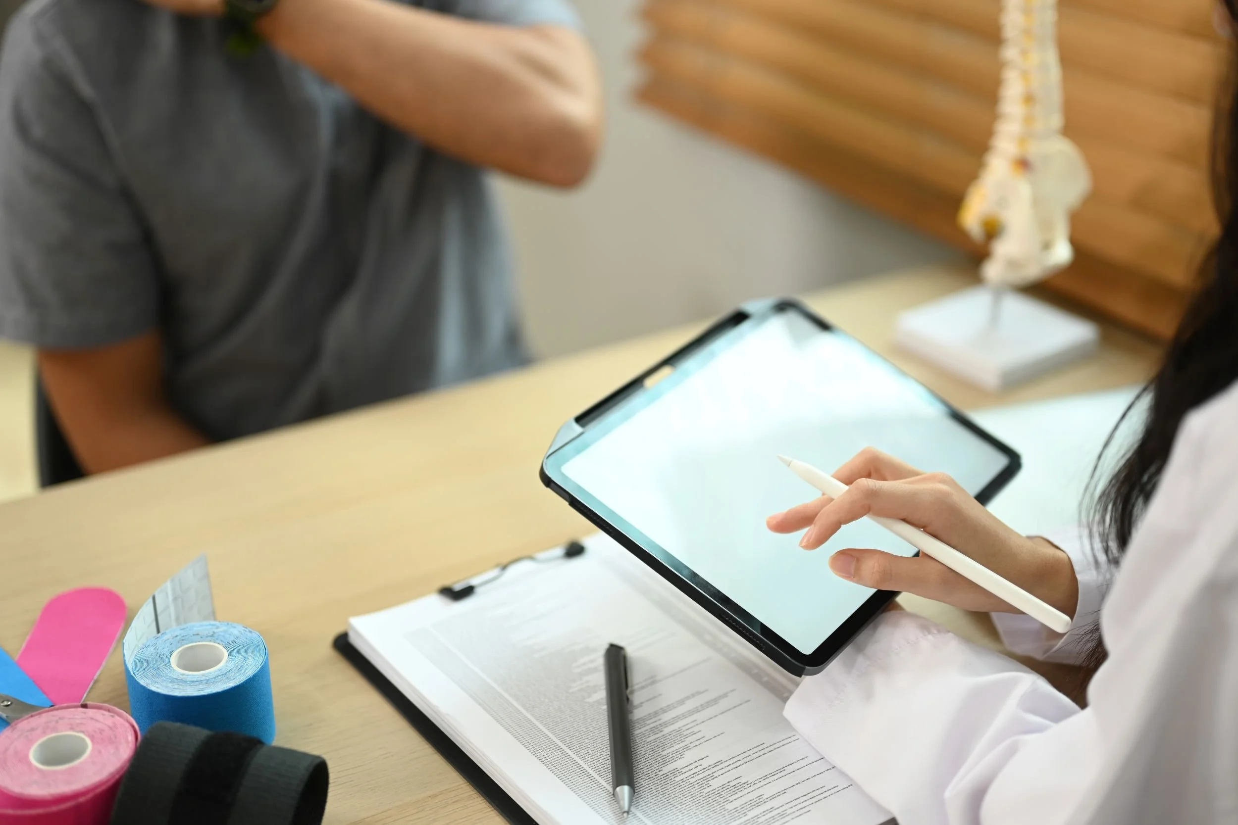 Person holding a tablet and stylus with various colored rolls of tape and notebooks on the desk.