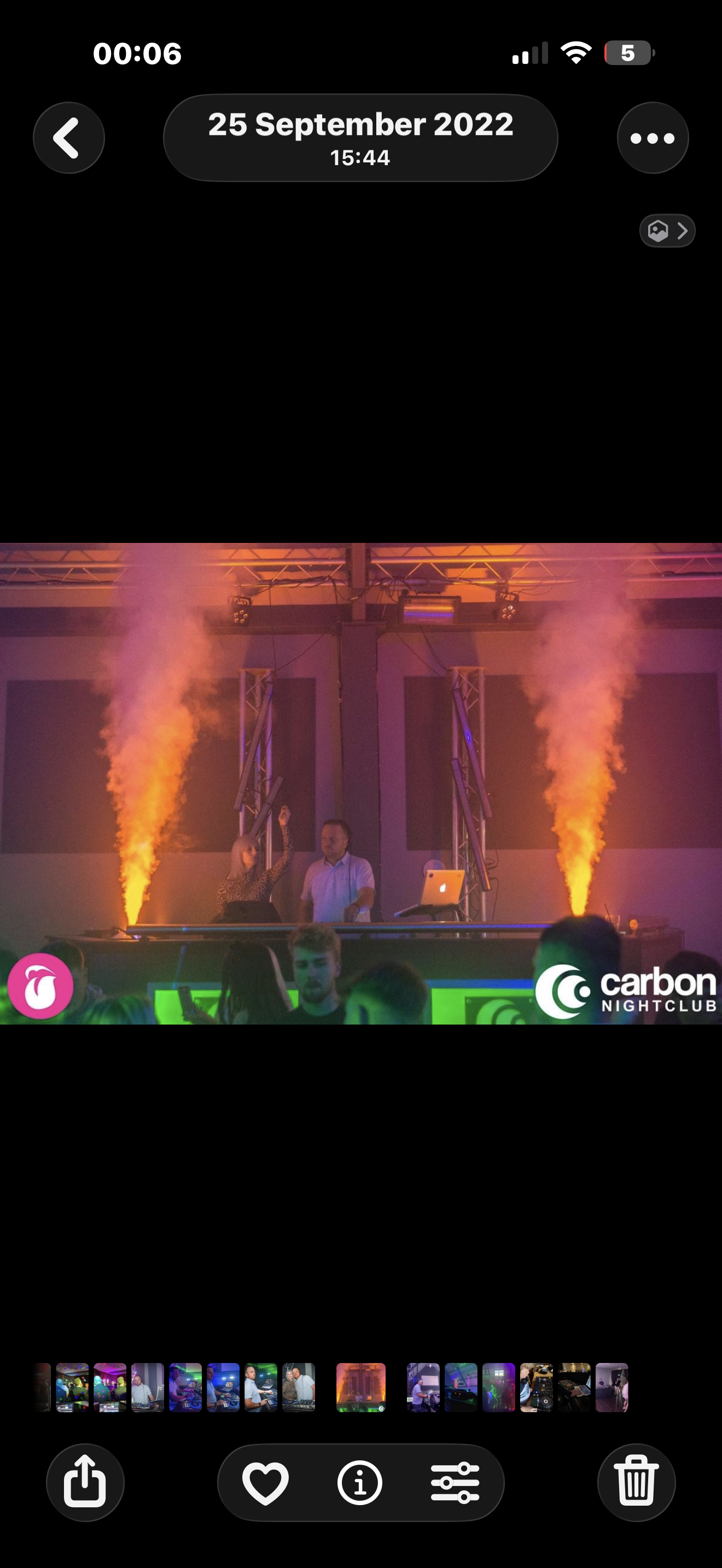 A scene from a nightclub featuring a DJ at the booth with smoke machines emitting orange smoke, colorful lighting, and a crowd dancing. The logo for Carbon Nightclub is visible in the bottom right corner.