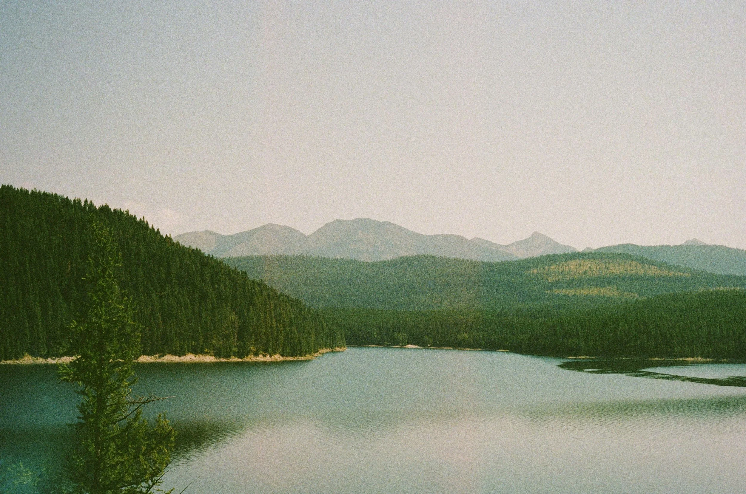 A scenic view of a lake surrounded by forested mountains with a few clouds in the sky.