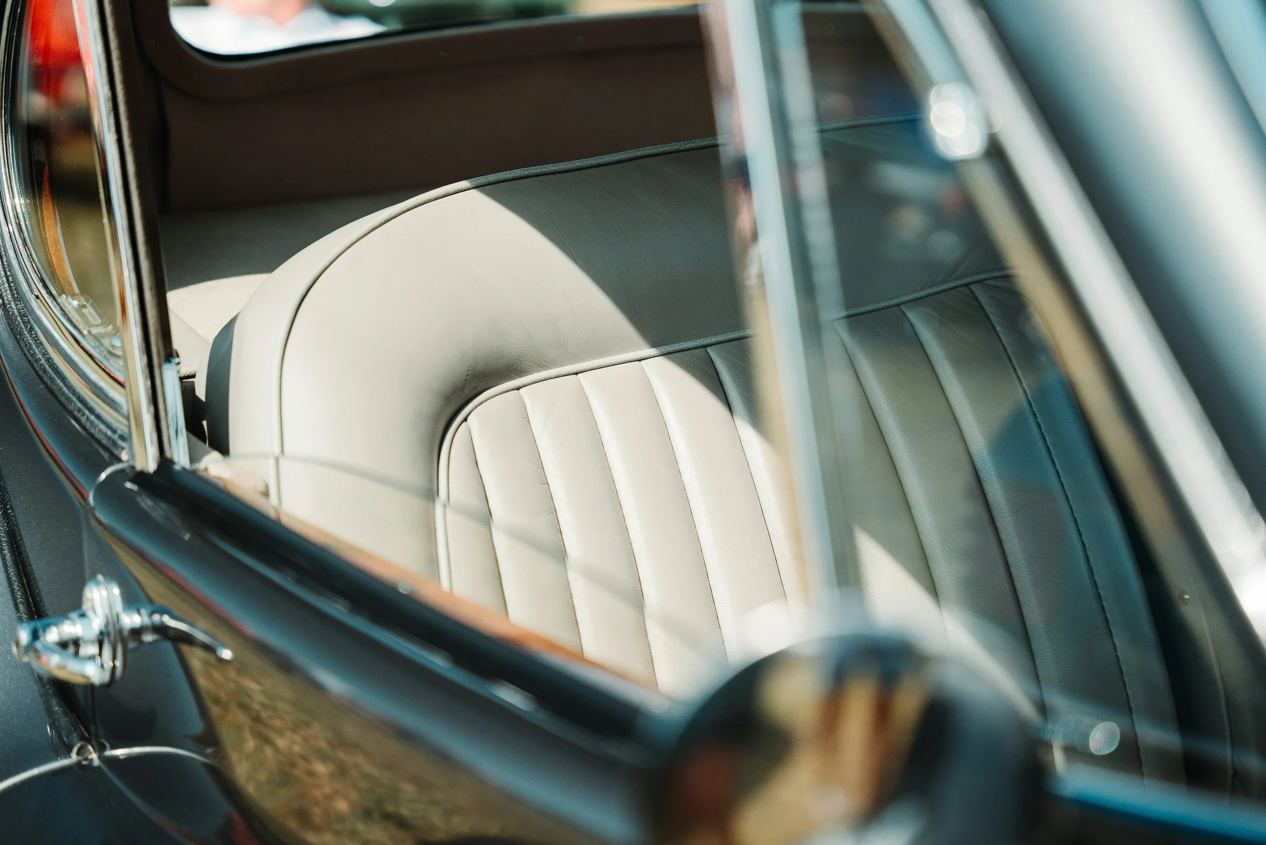 Close-up of the interior of a vintage car, showing the beige leather seats and a partial view of the steering wheel through the open window.