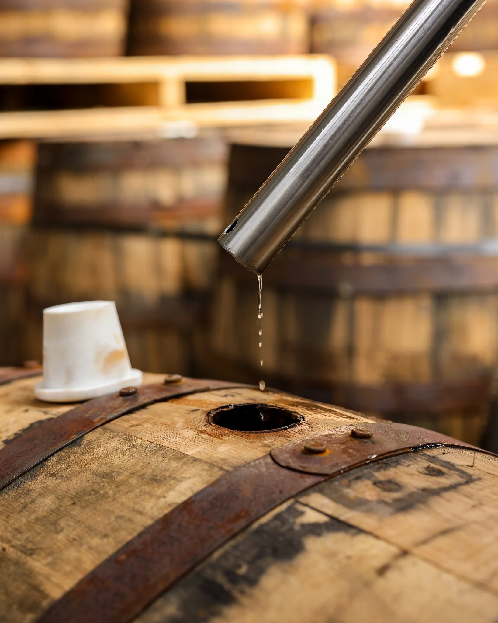 Close-up of a wooden barrel with a metal tap, with water dripping into a cup below in a brewery or distillery setting.