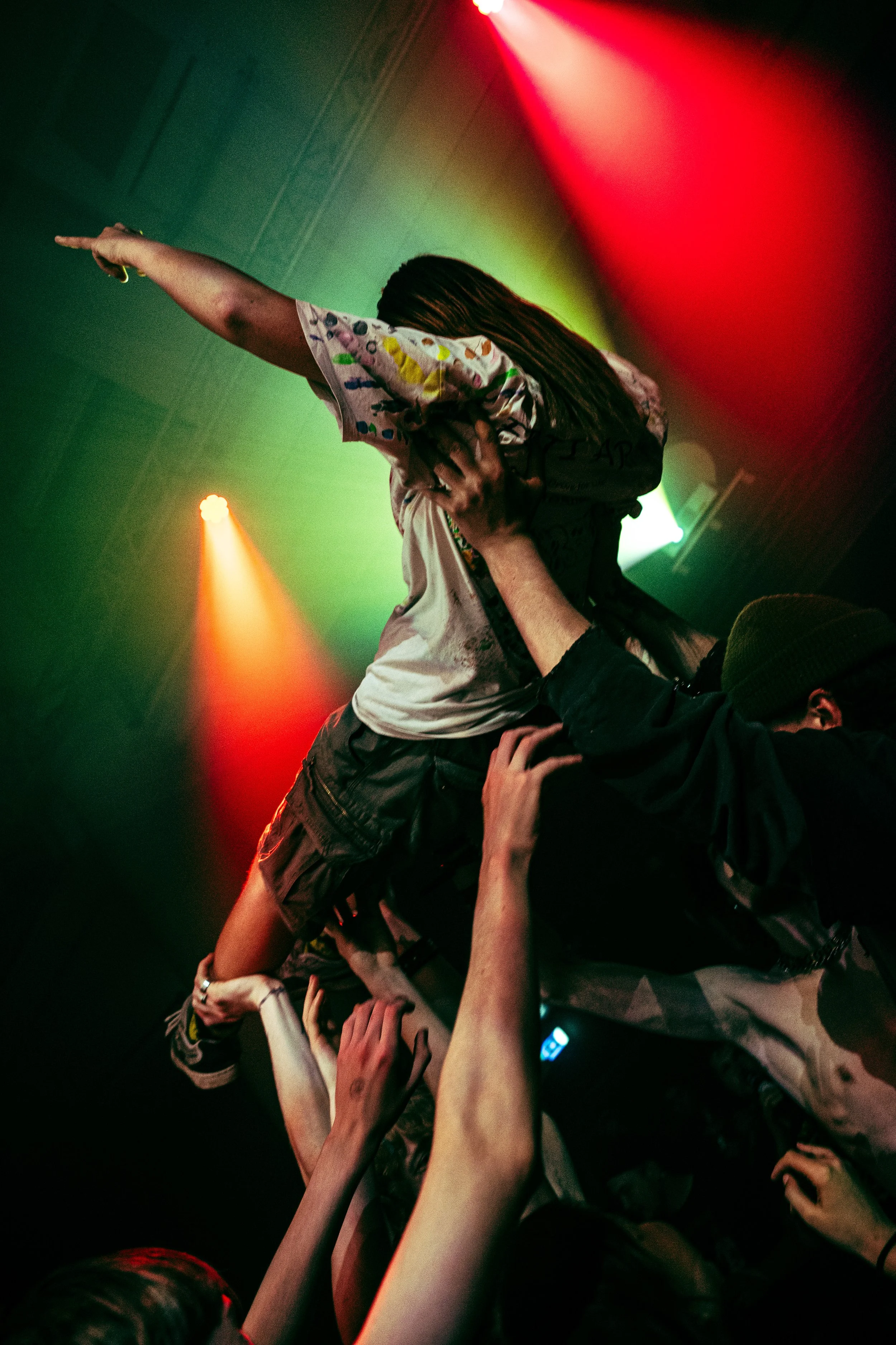 People on stage at a concert, some reaching out their hands, with colorful stage lights illuminating the scene.