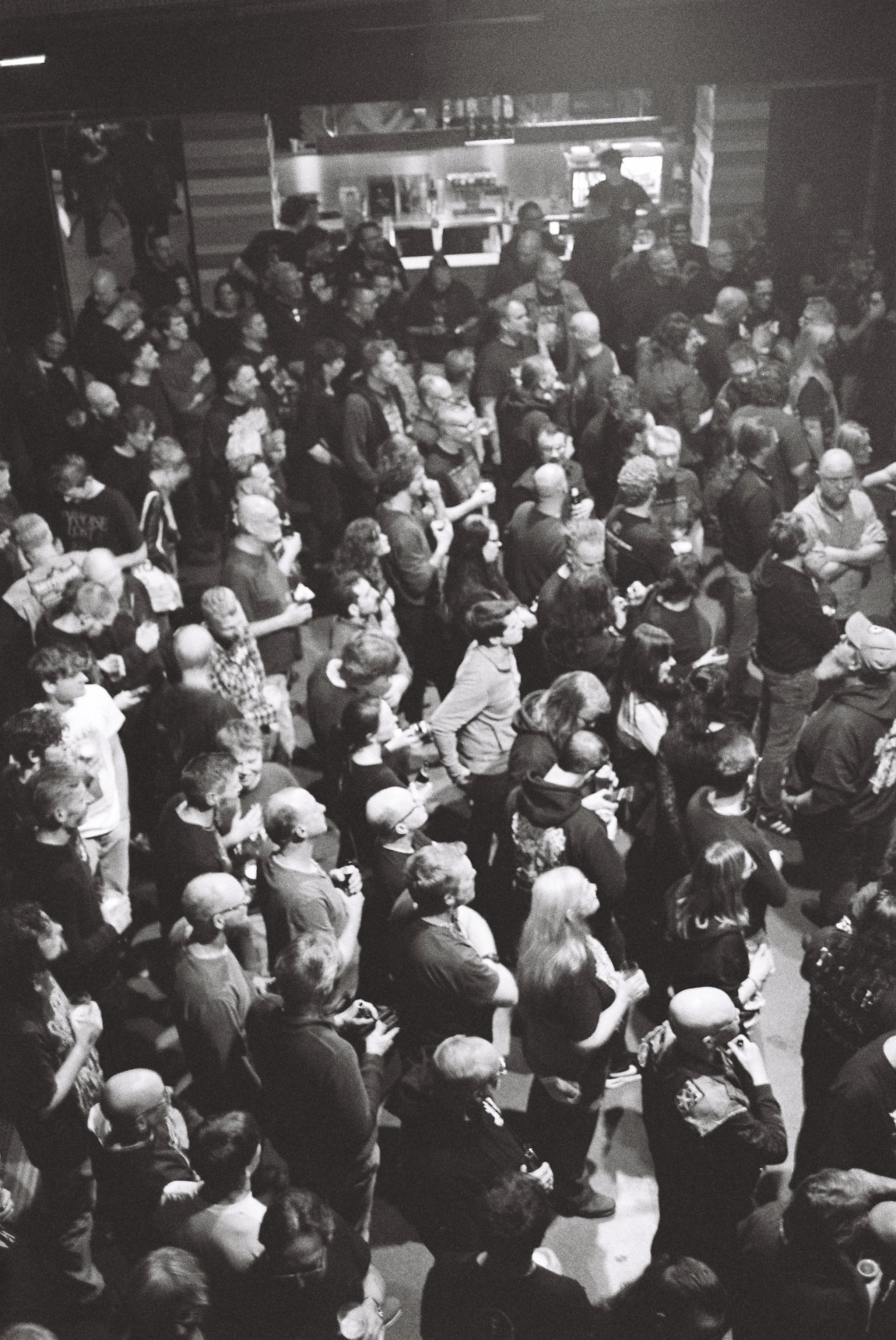A large crowd of people standing indoors, many wearing face masks, seemingly attending an event.