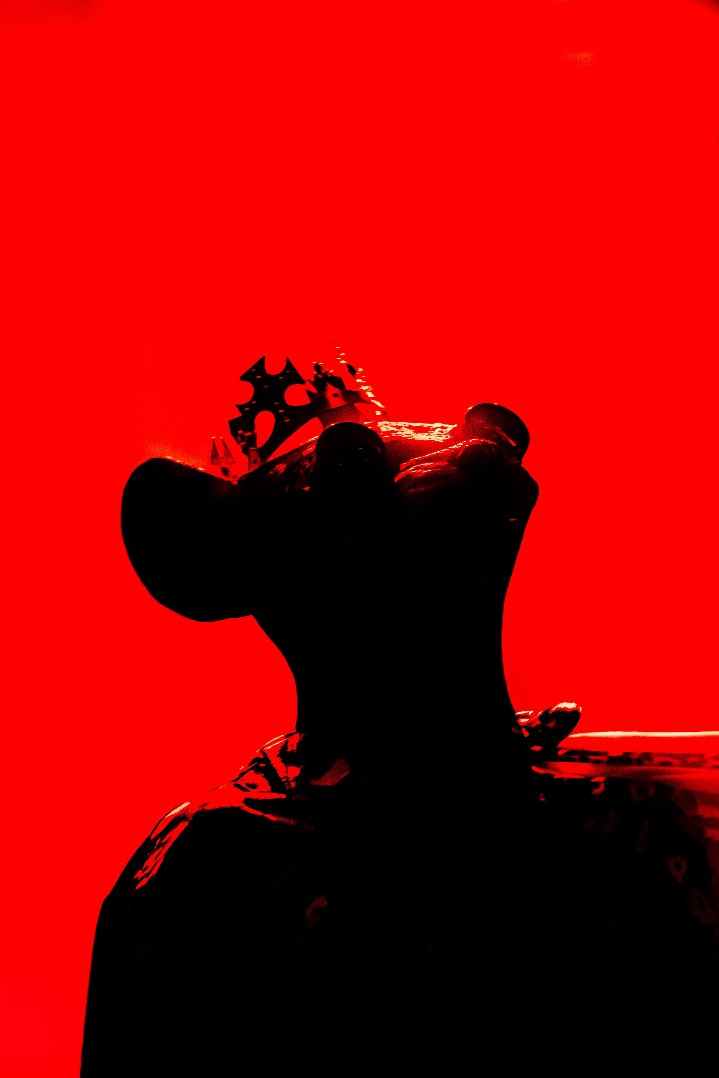 Silhouette of a person holding a crown against a red background.