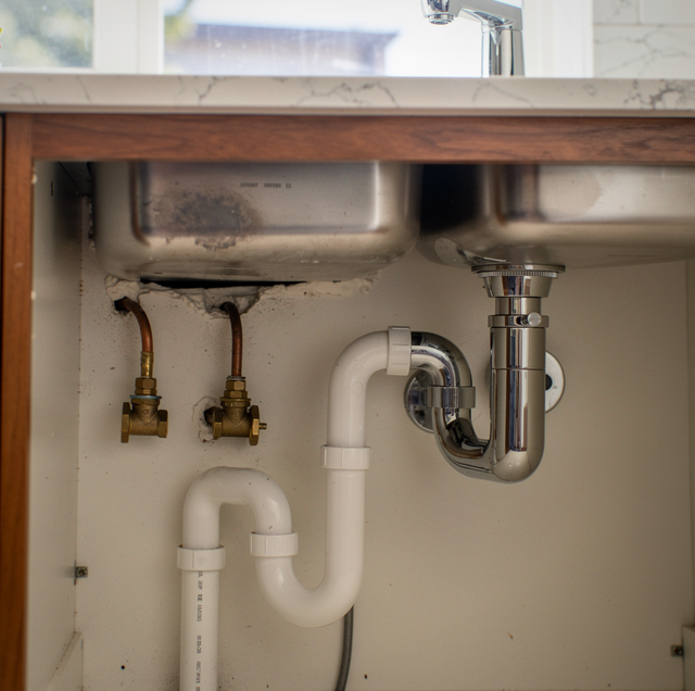 two tradesmen comparing tools beside open under-sink cabinet
