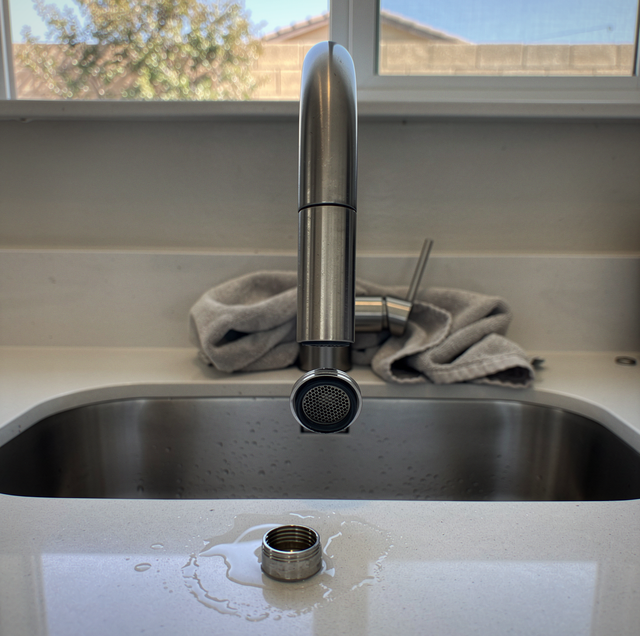 A metal faucet with aerator stands over a kitchen sink on a windowsill with a cloth towel nearby.