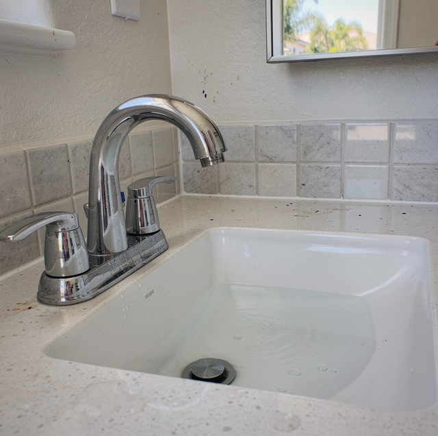 Chrome faucet and white sink with tile backsplash in a bathroom with window view.