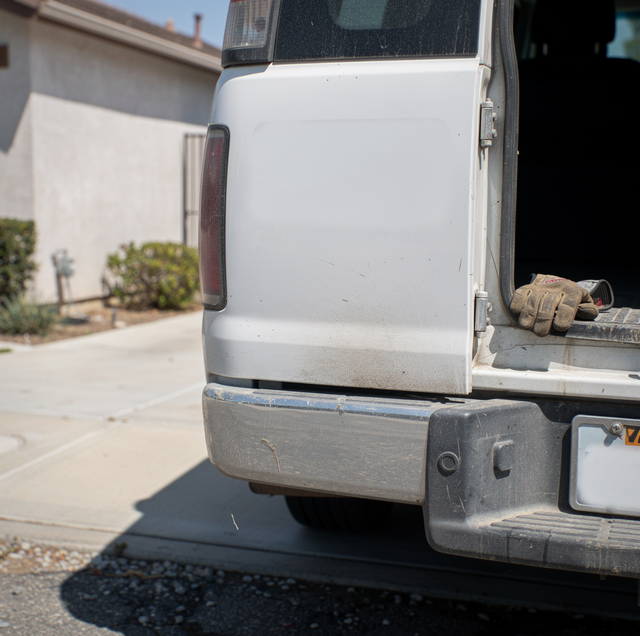 White pickup truck with contractor license decal and rolled blueprints on roof rack parked in front of a house.