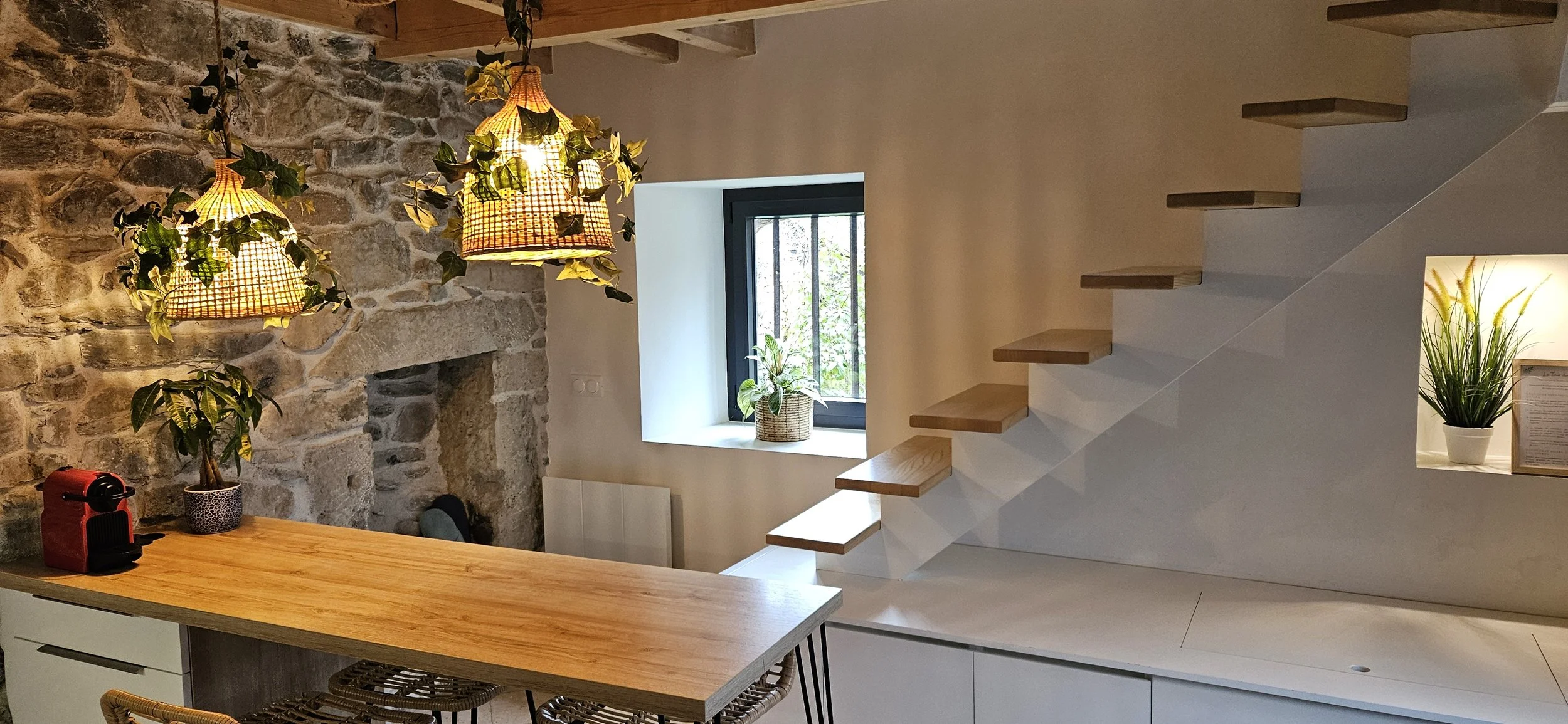 Intérieur rénové avec mur en pierre, escalier en bois et plantes, éclairage suspendu chaleureux