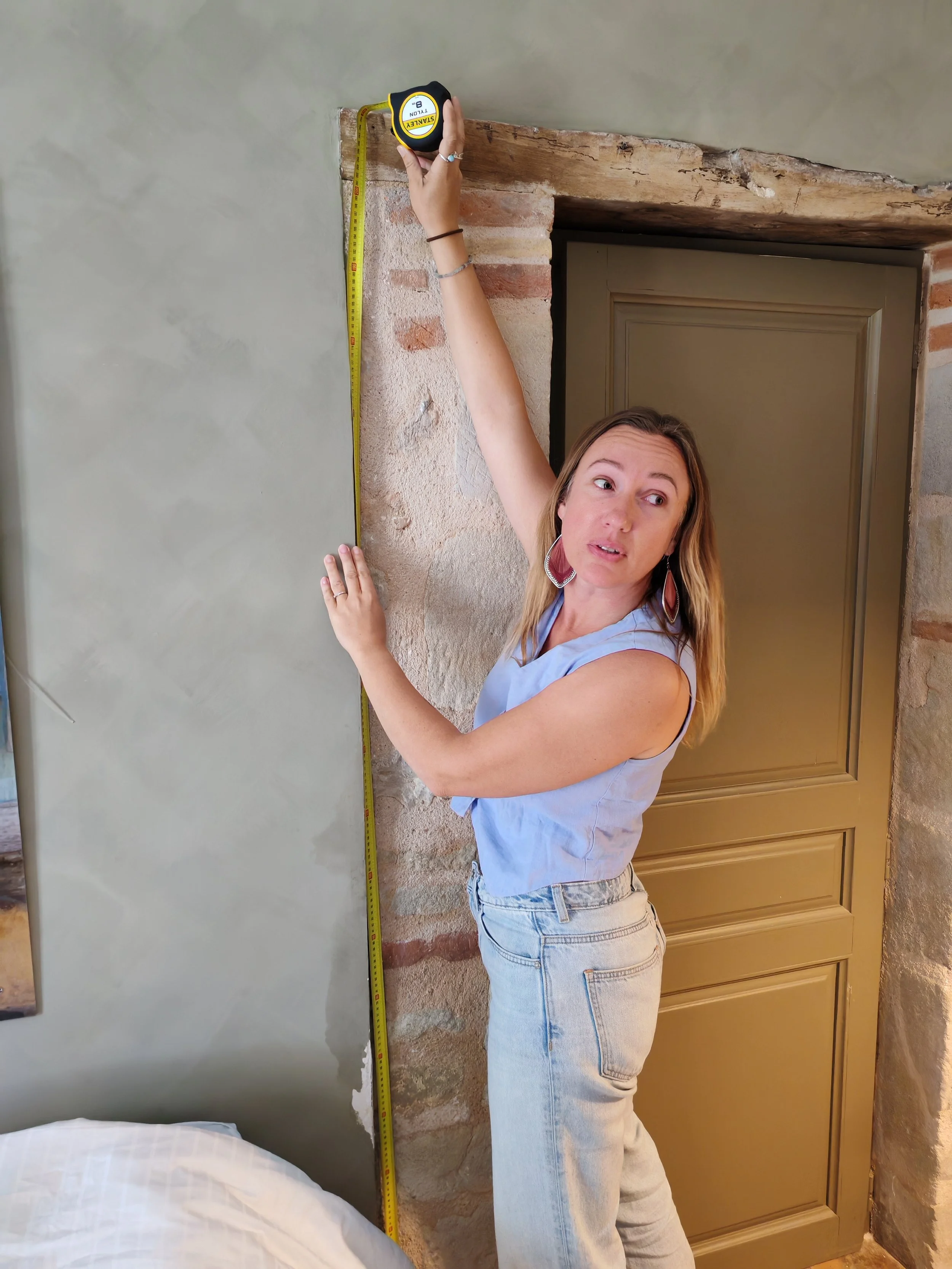 Amandine réalise un relevé de mesures sur un mur de briques dans le cadre d'un projet de rénovation