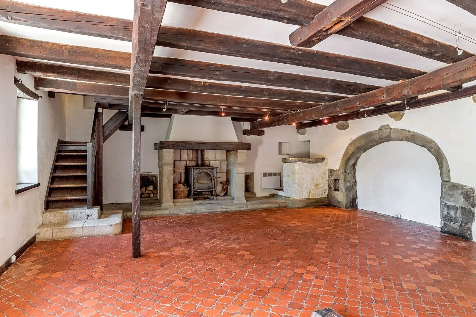 Salon rustique avec cheminée en pierre, poutres apparentes et sol en terracotta, visite conseil avant travaux