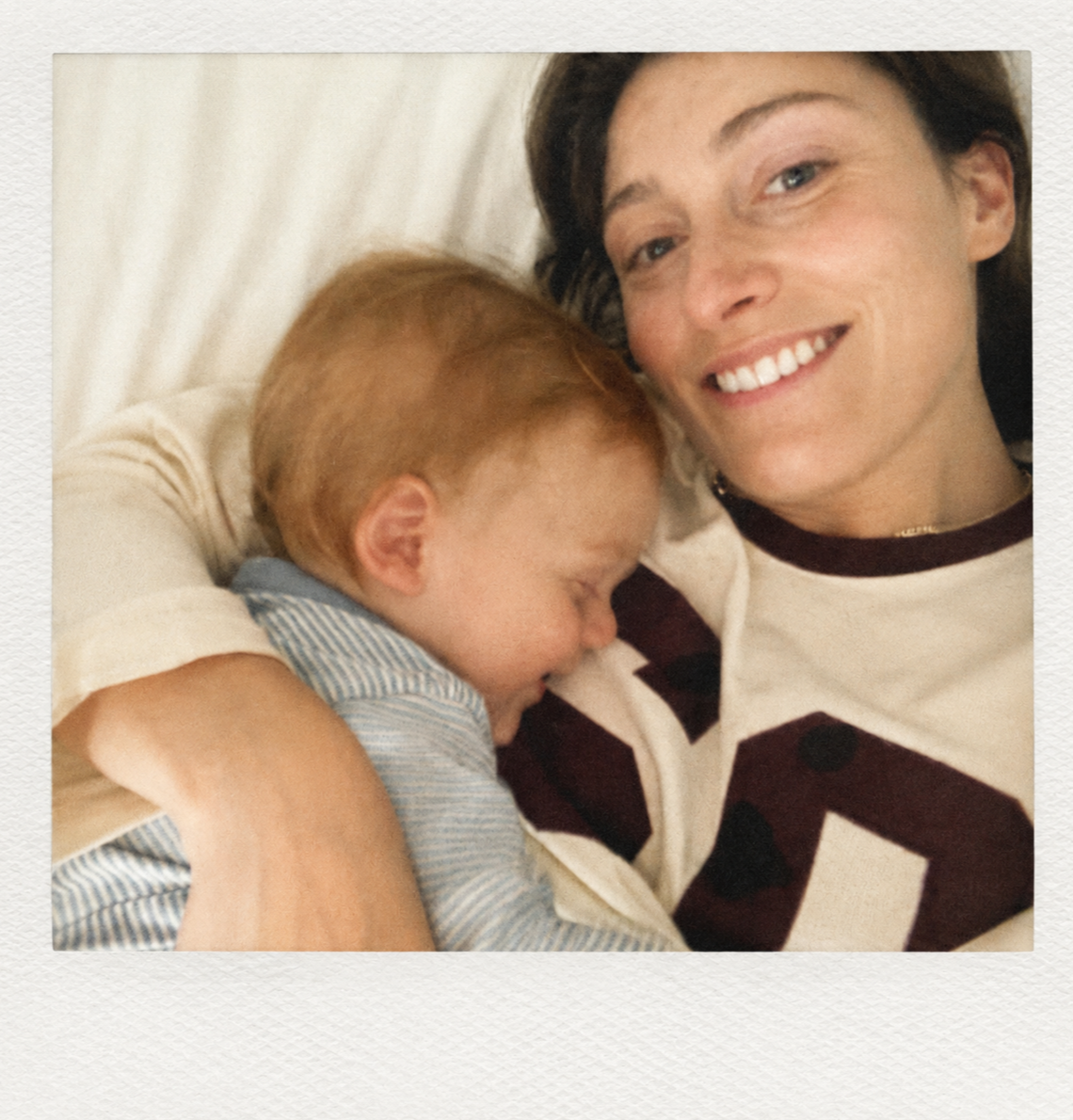 A woman and a young boy lying in bed together, smiling and cuddling.