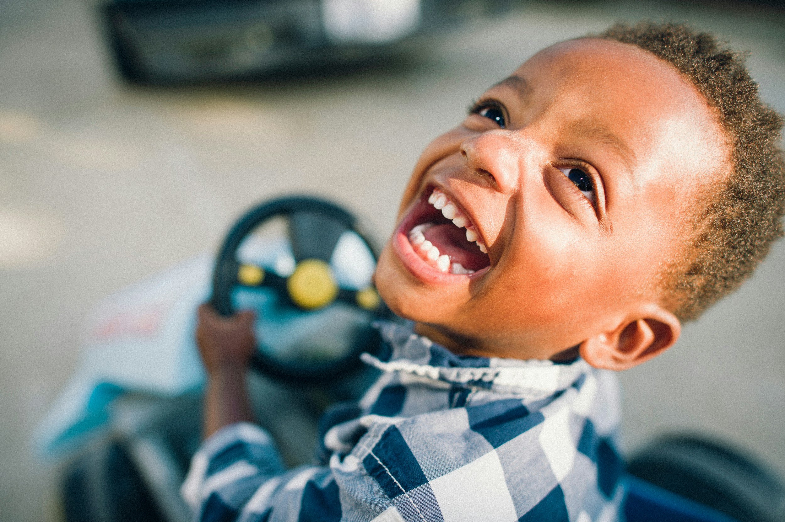 A young child with curly hair smiling joyfully, holding an object, wearing a striped shirt.