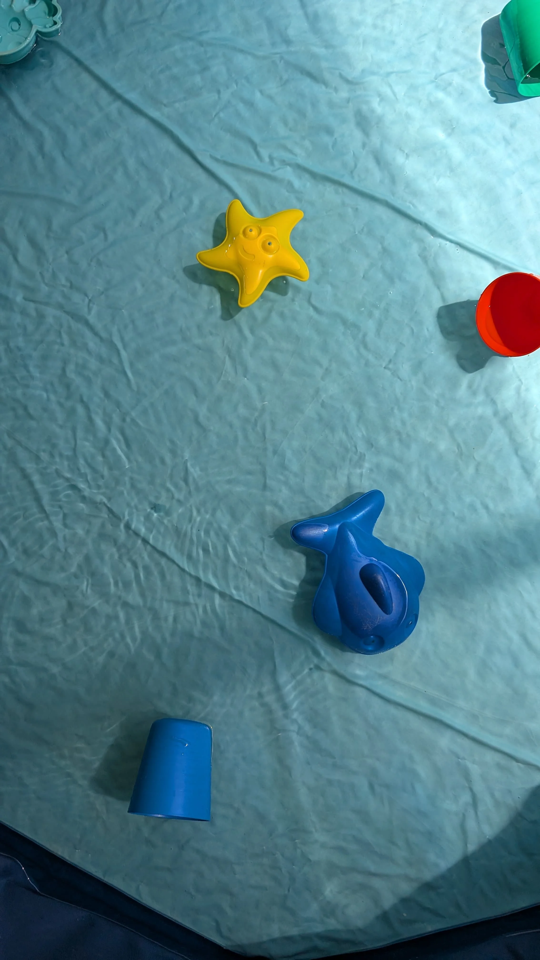 Colorful floating toys and cups on a blue surface.