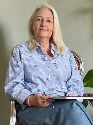 A mature female psychotherapist with white hair sitting in a chair in the therapy room.