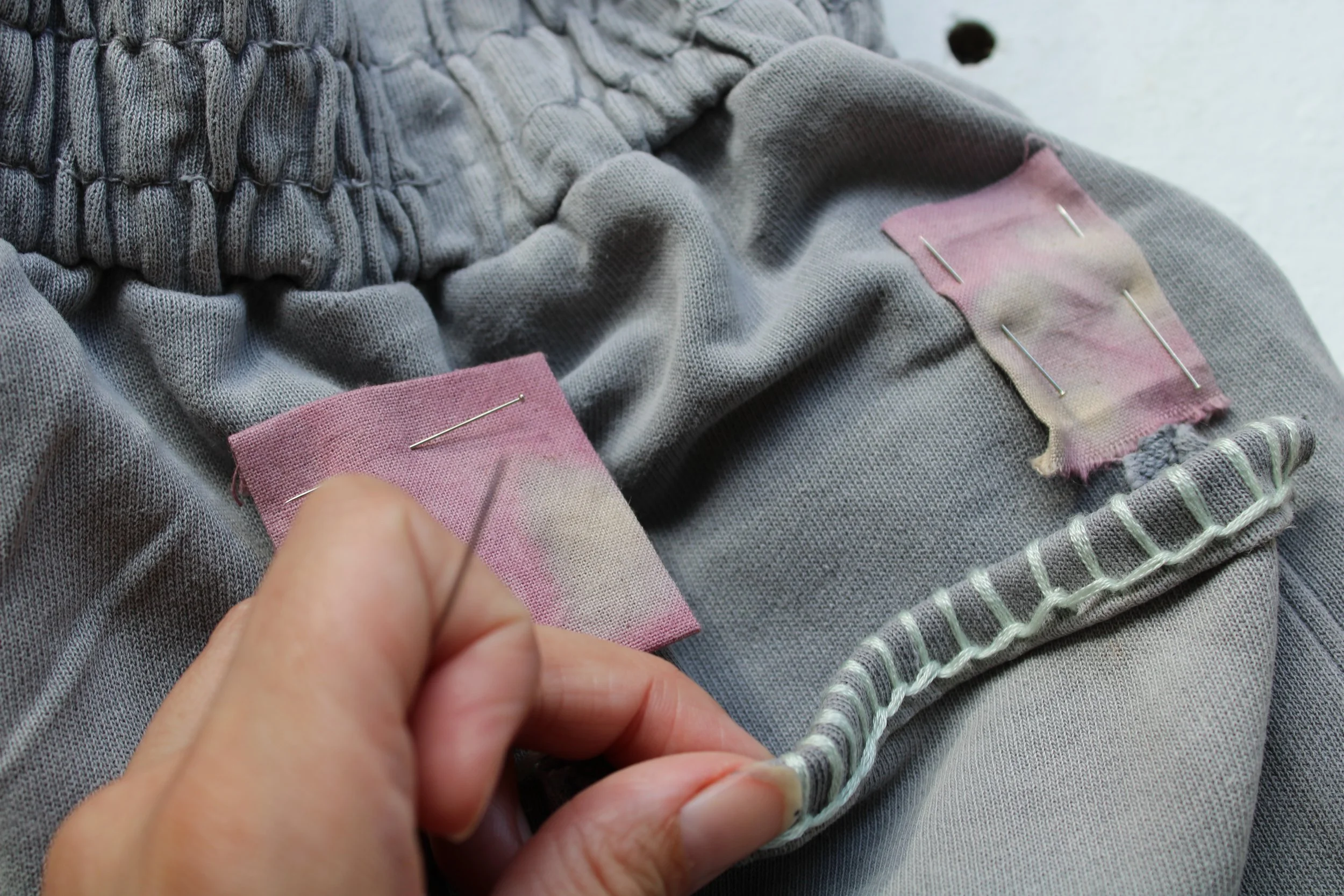 Close-up of a person sewing two pieces of pink fabric together with pins on dark gray and striped fabric.