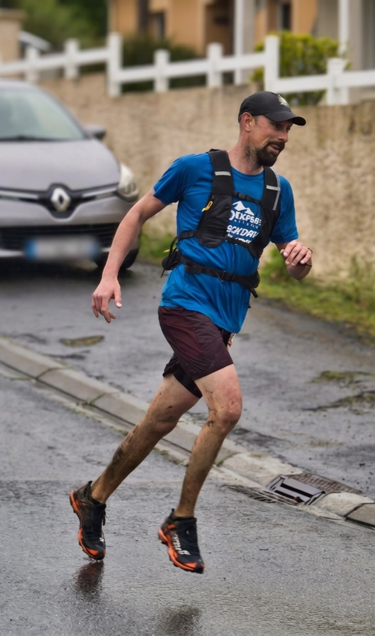Un homme court sur une route mouillée, vêtu d'un t-shirt bleu, shorts marron, portant un sac à dos, avec des vêtements mouillés et un paysage résidentiel en arrière-plan.