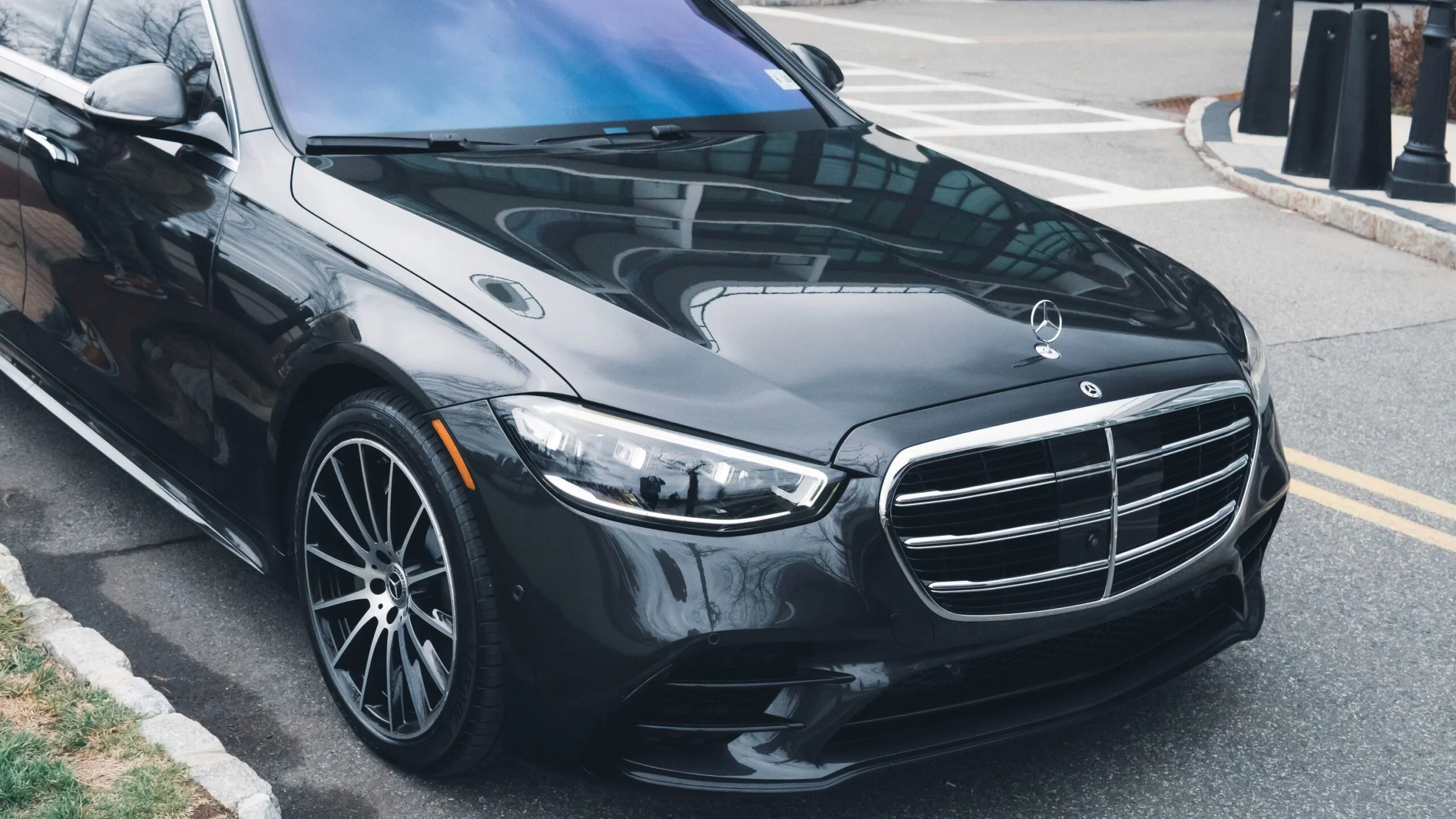 Black luxury Mercedes-Benz car parked on the street near a sidewalk with black bollards.