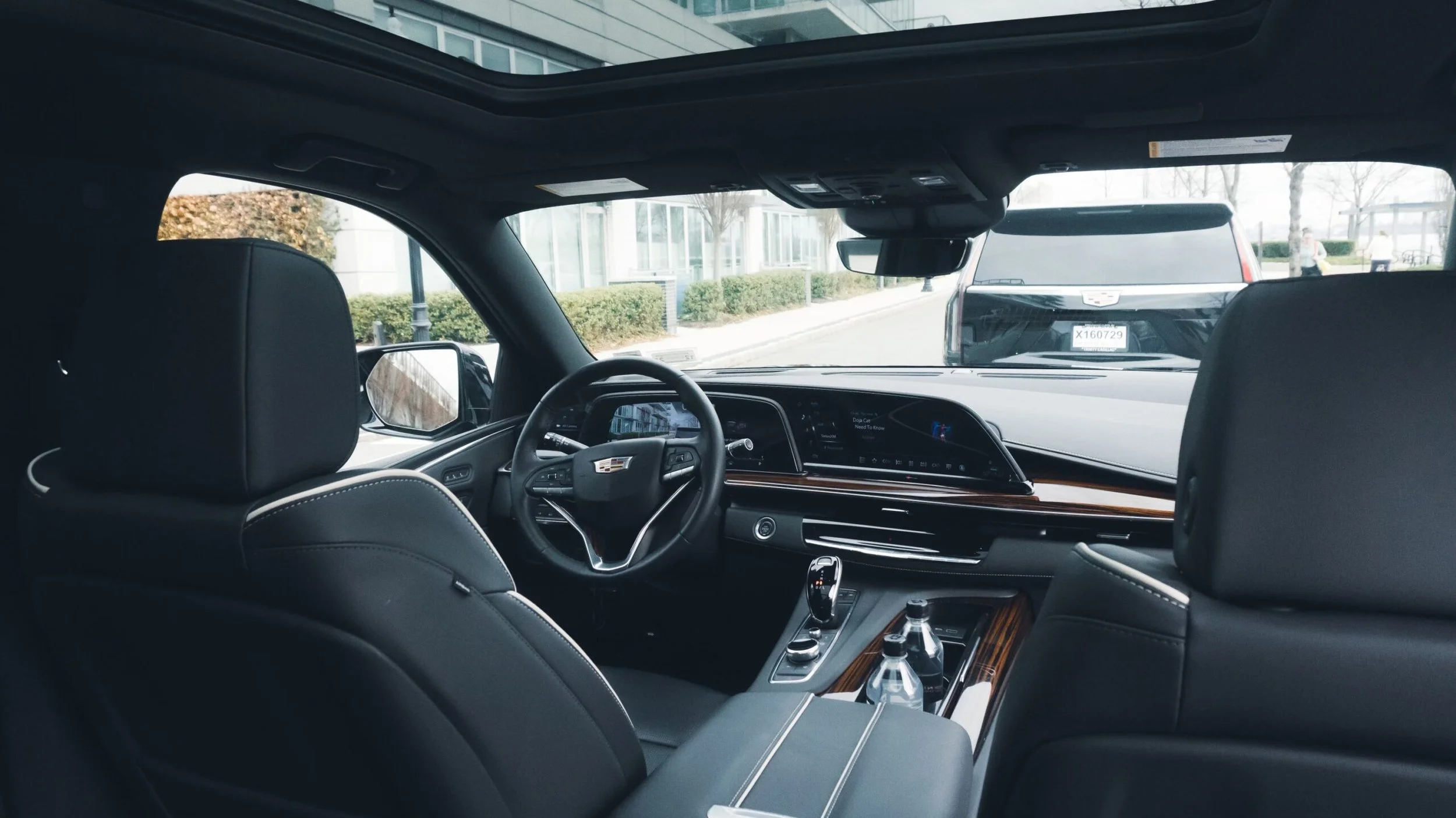 Interior view of a luxury Cadillac vehicle's front seats and dashboard, with a parking lot and other cars visible through the windshield.