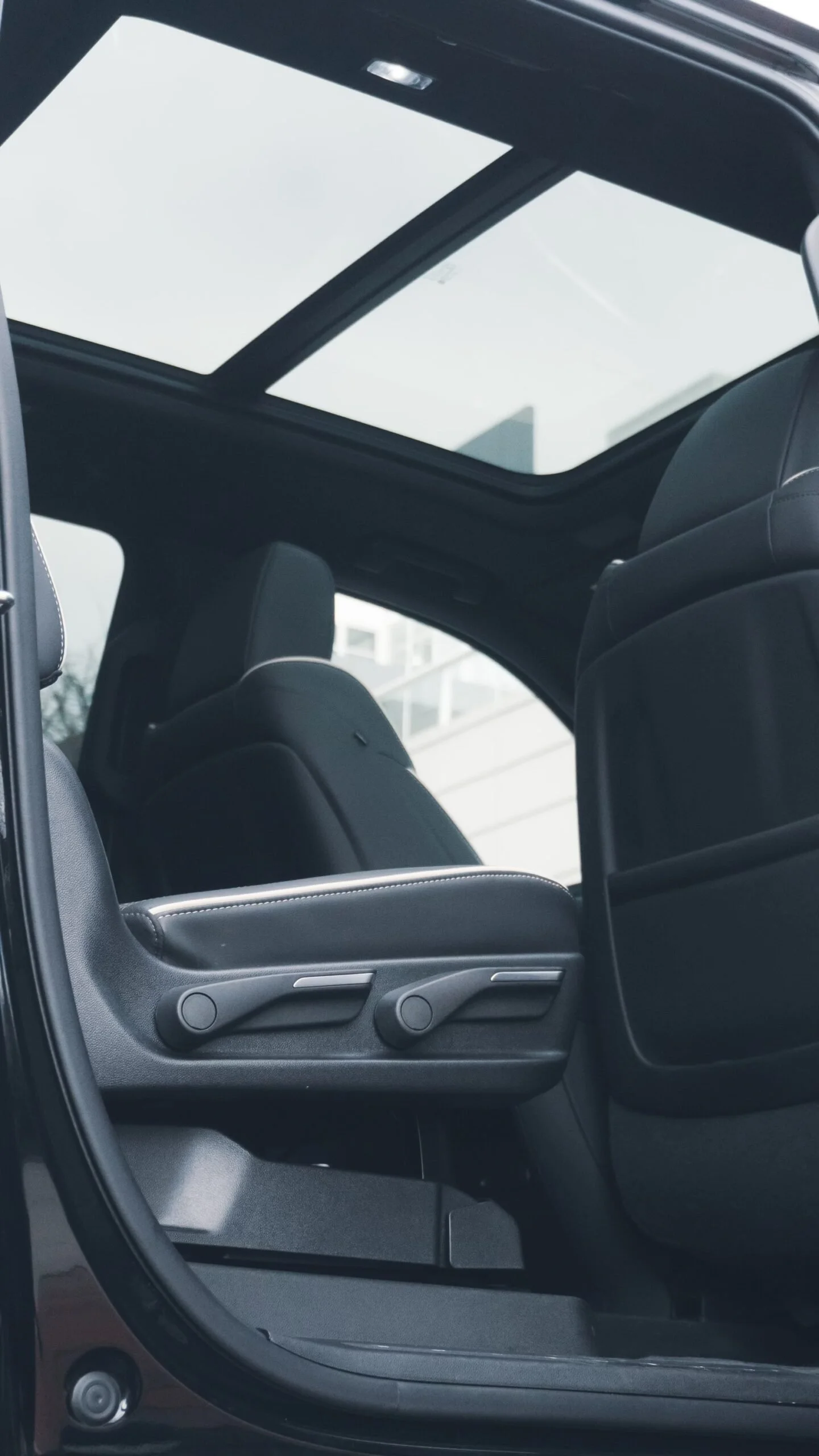 View from the open door of a car showing the interior with black leather seats and window with a building in the background.