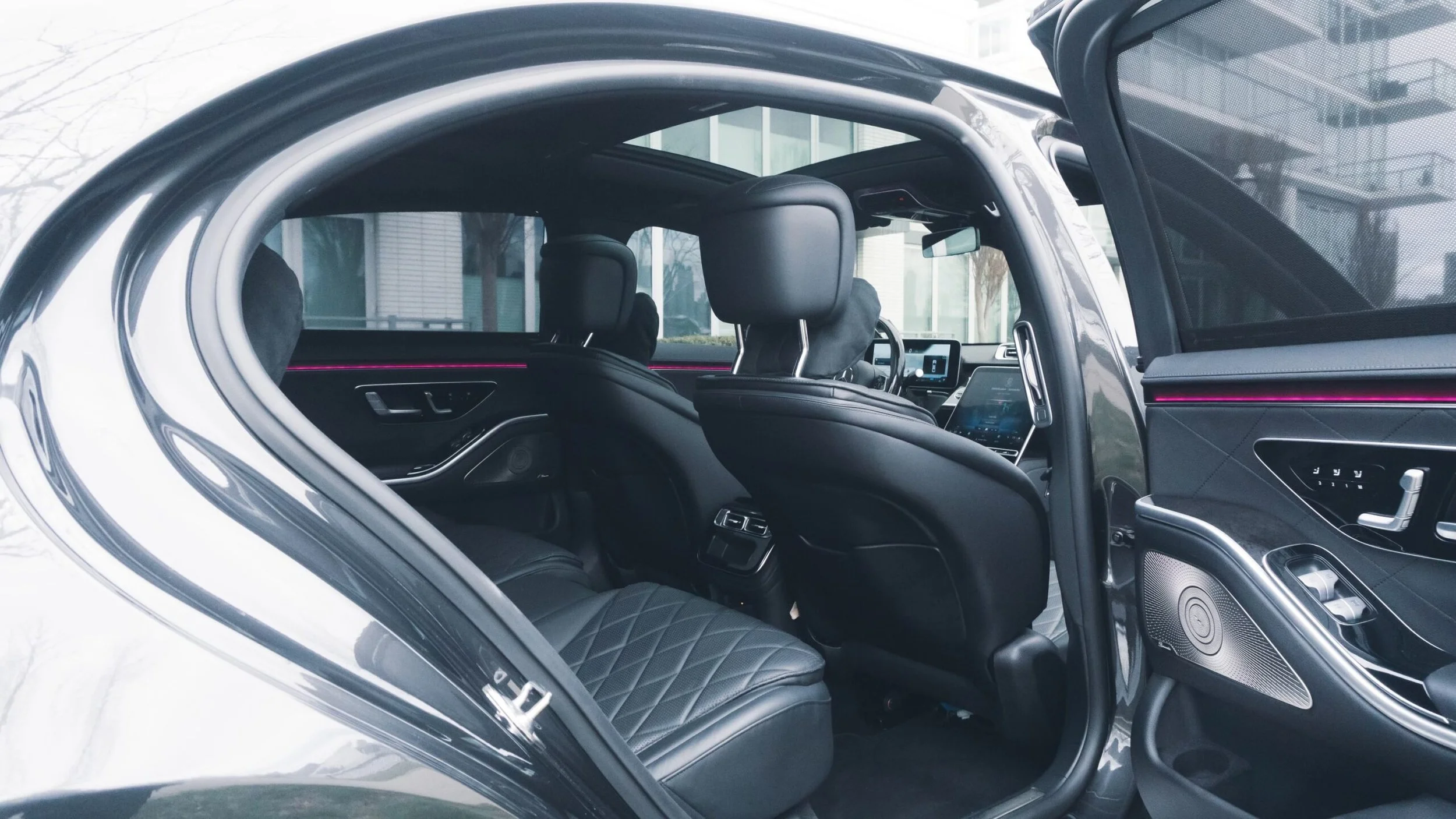 Interior of a modern electric vehicle with black leather seats, digital dashboard, and ambient lighting, viewed through a partially open door.
