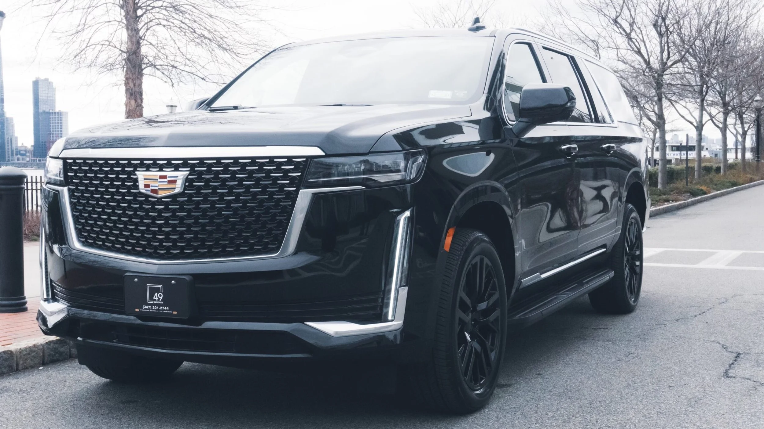 Black Cadillac SUV parked on a city street with trees and buildings in the background.