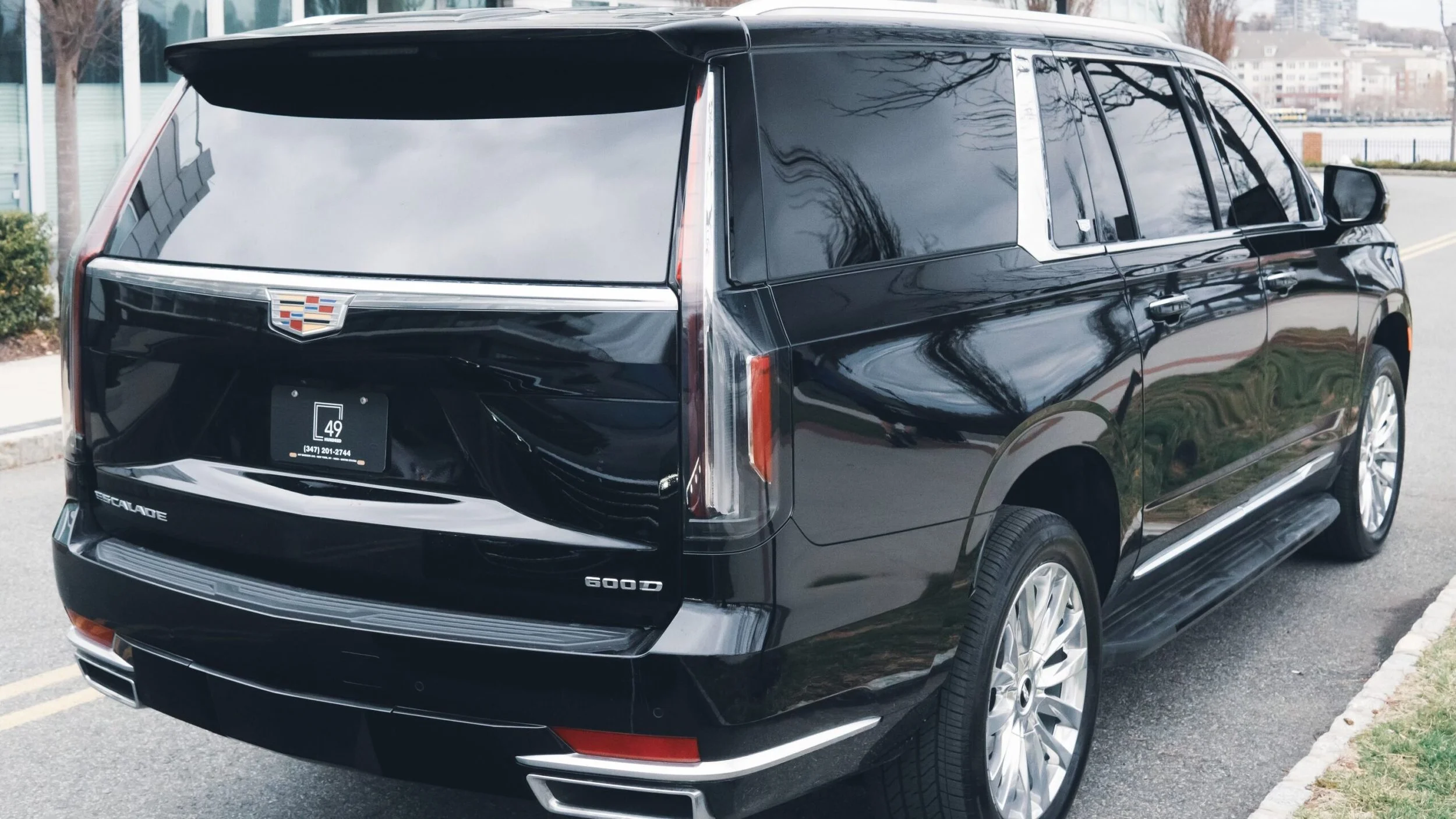 Black Cadillac Escalade parked on a city street, with reflections of nearby buildings and trees on its surface.