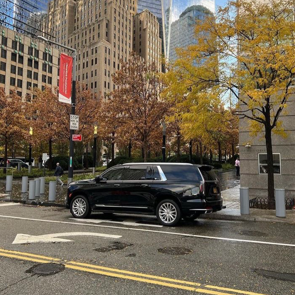 A black luxury SUV parked on the street with autumn trees in the background inside a city with modern high-rise buildings.
