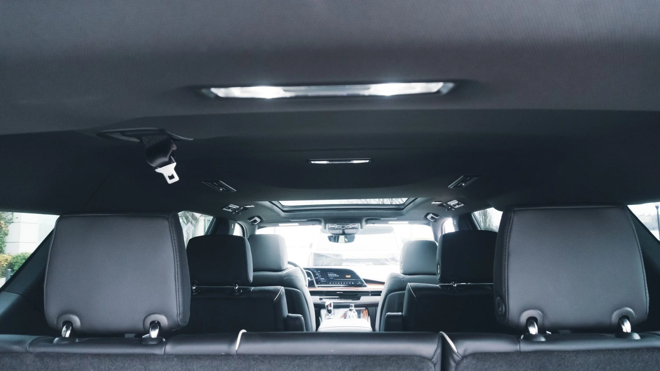 Interior of a modern vehicle, showing the back of the front seats and the dashboard with an infotainment screen, with additional seats and windows visible at the rear.