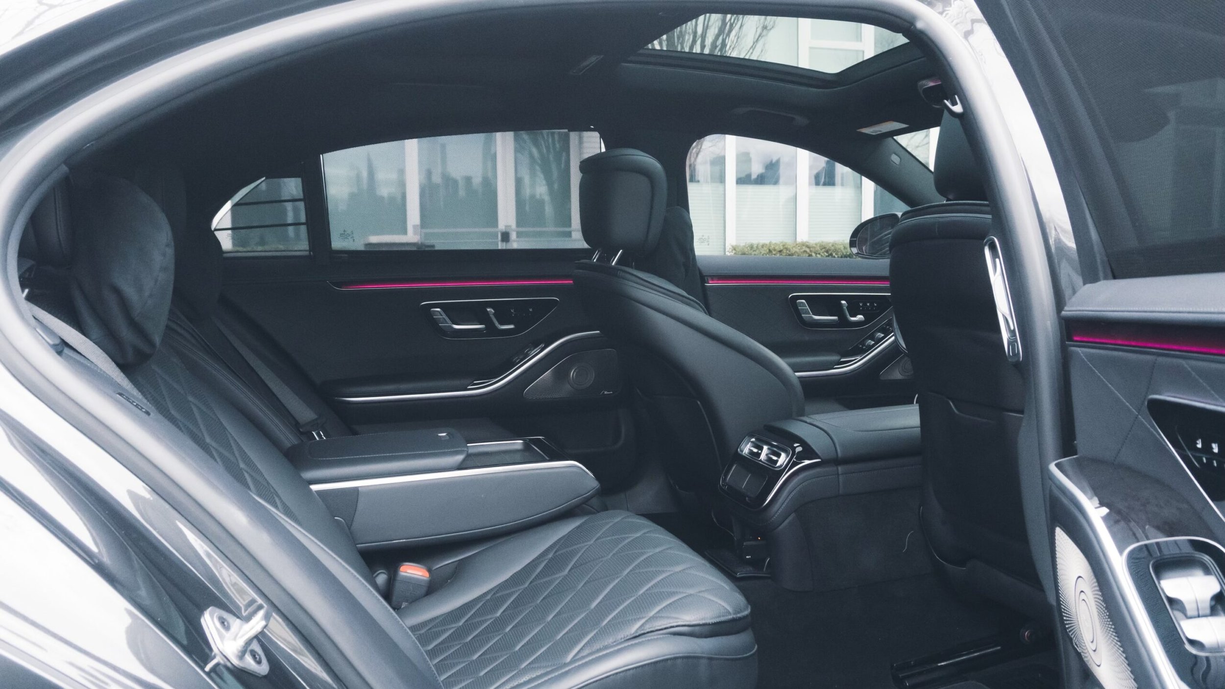 Interior of a luxury car with black leather seats and pink ambient lighting, visible from the open door.