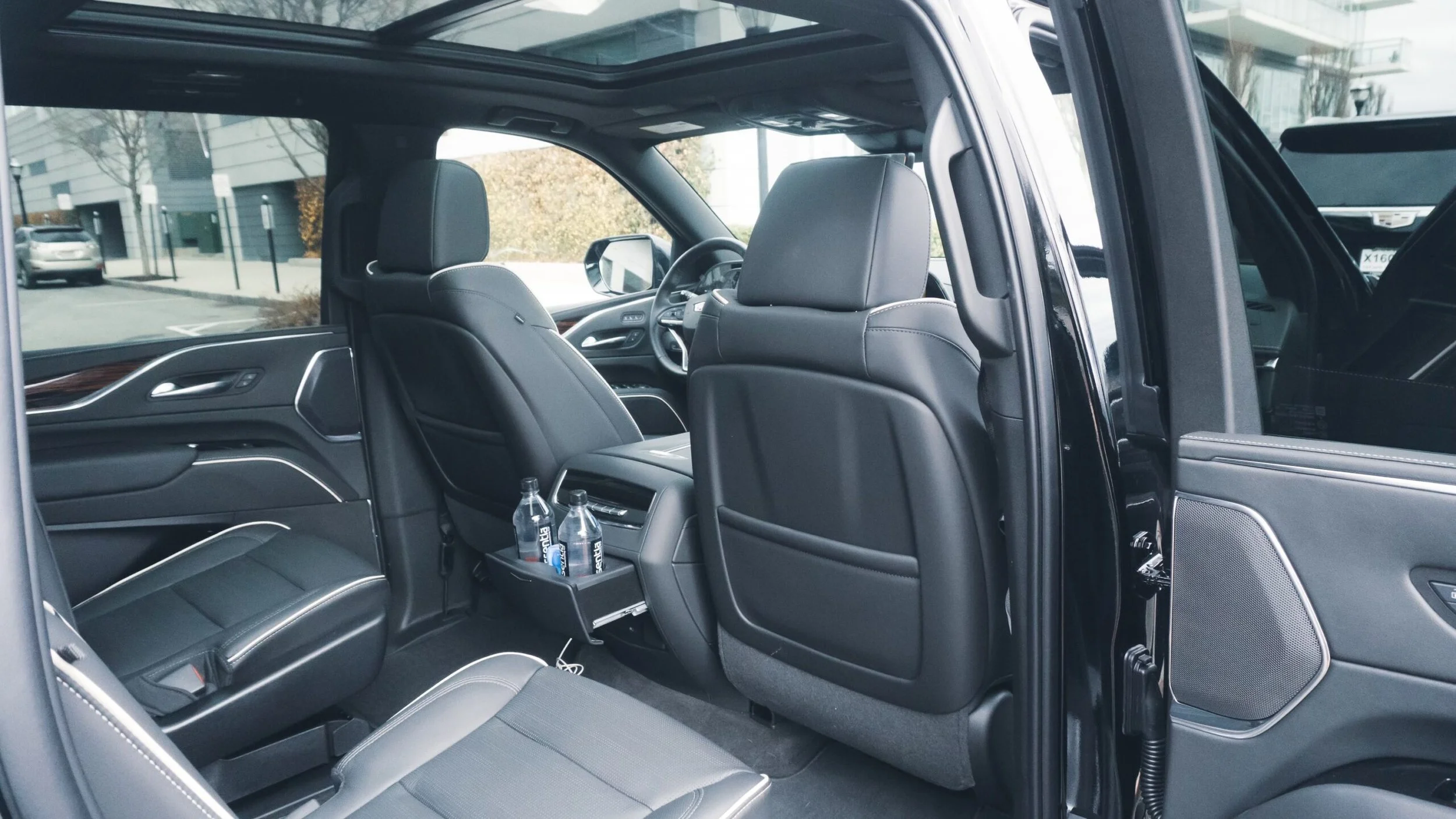 Interior of a black luxury SUV showing the back seats, front seats, and the dashboard. Two water bottles are placed in the back seat cup holder.