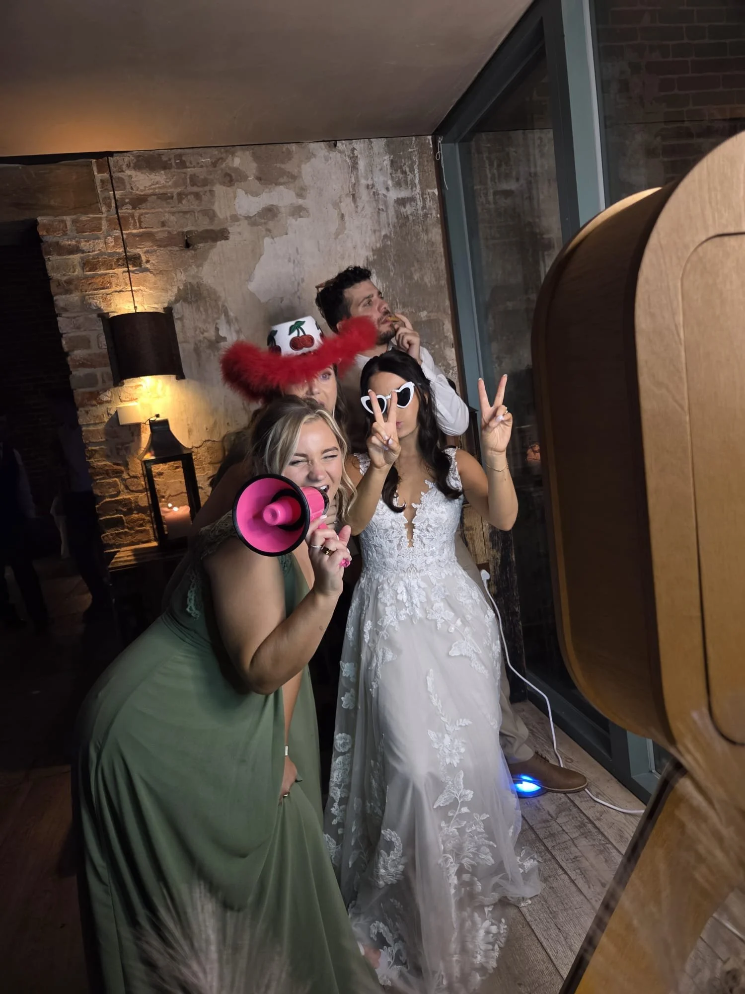 Friends posing at a photo booth hire event, exposed brick backdrop in Cambridgeshire