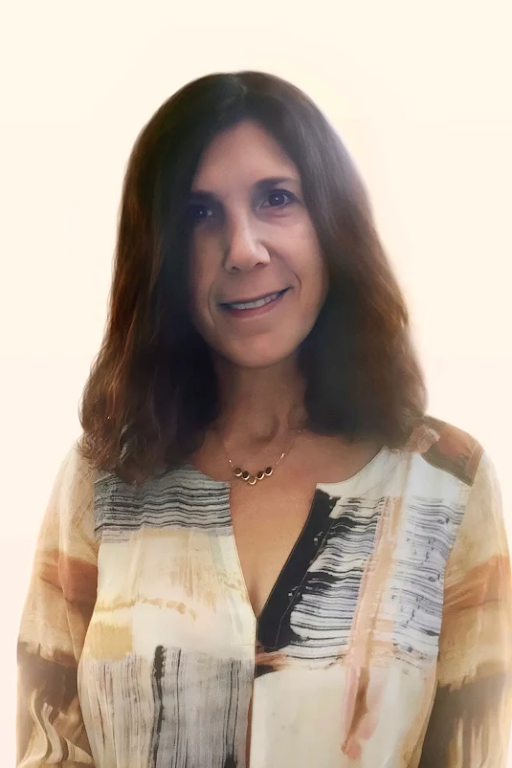 A woman with shoulder-length brown hair wearing a patterned blouse and a necklace, smiling at the camera against a plain light background.
