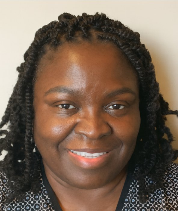 Close-up of a smiling woman with dark skin and twisted hairstyle, wearing a black patterned top, against a plain light background.