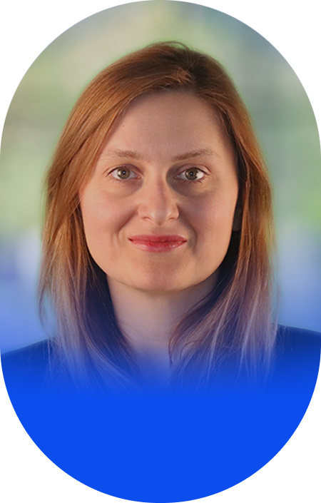 Headshot of a woman with red hair and a slight smile, set against a blurred background.