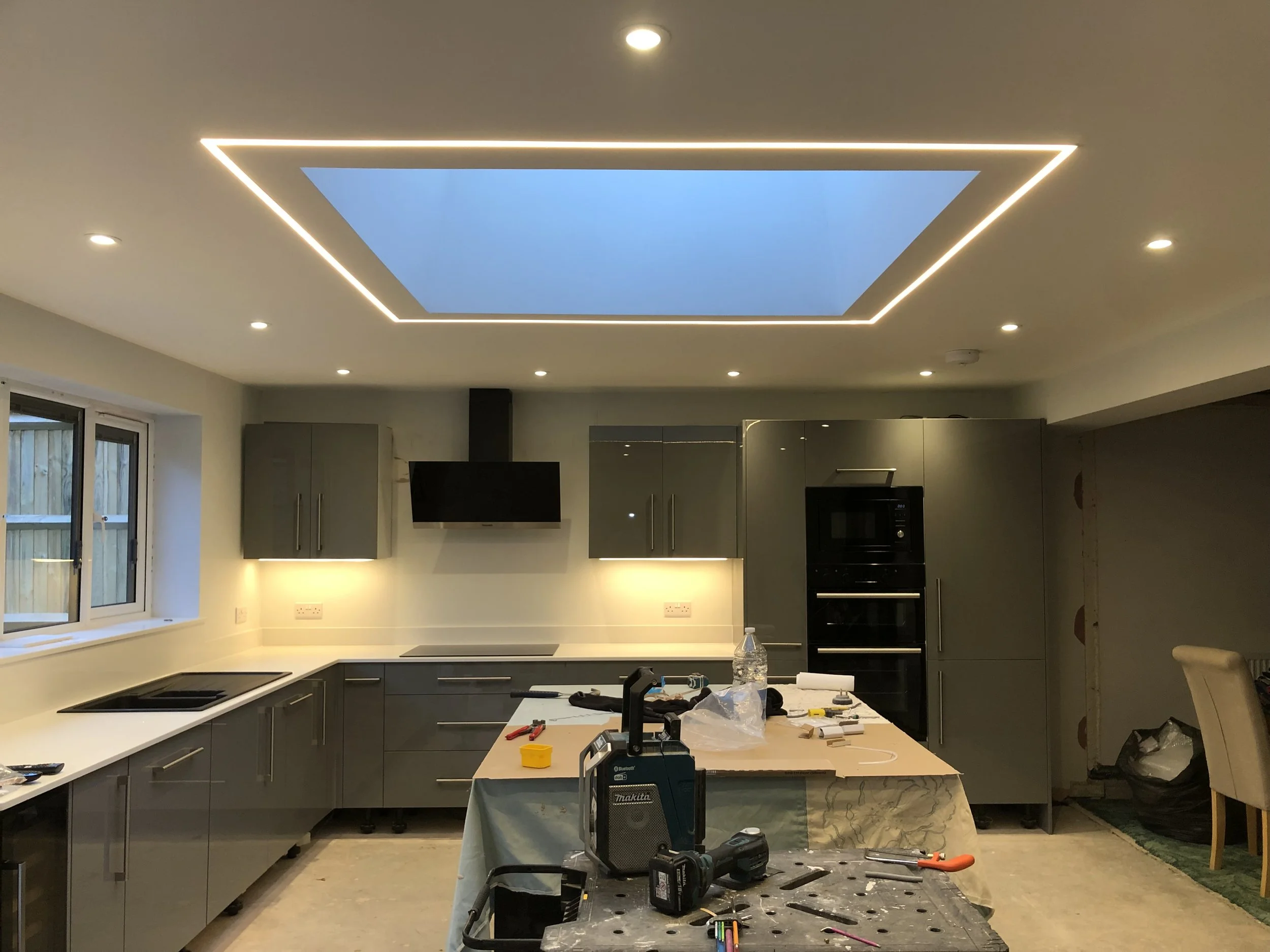 Modern kitchen with gray cabinets, a large center island, a skylight, and ongoing construction with tools and supplies on the island and nearby table.