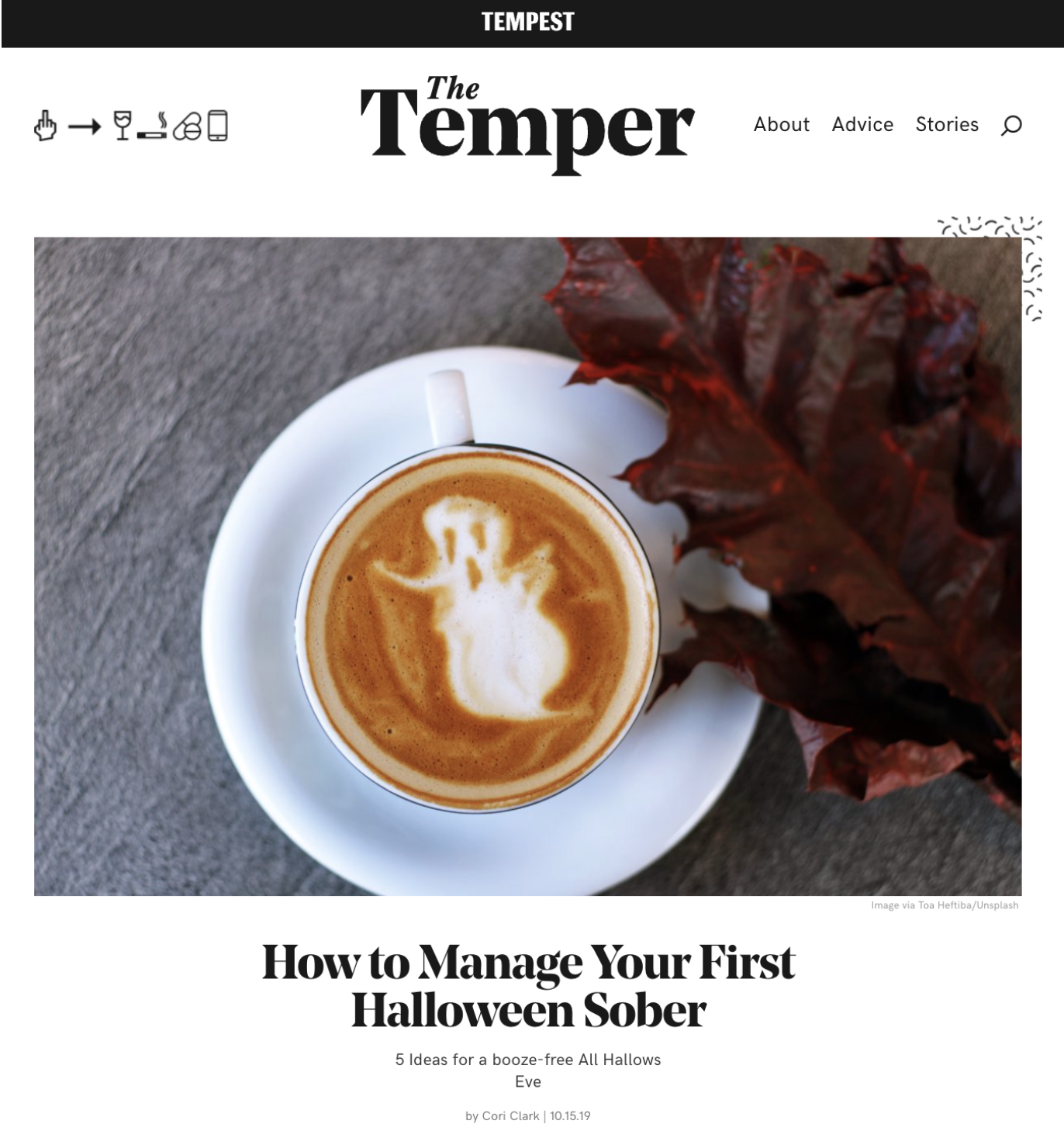 A white cup of coffee on a saucer with a latte art of a ghost against a gray surface, with a red autumn leaf on the side.