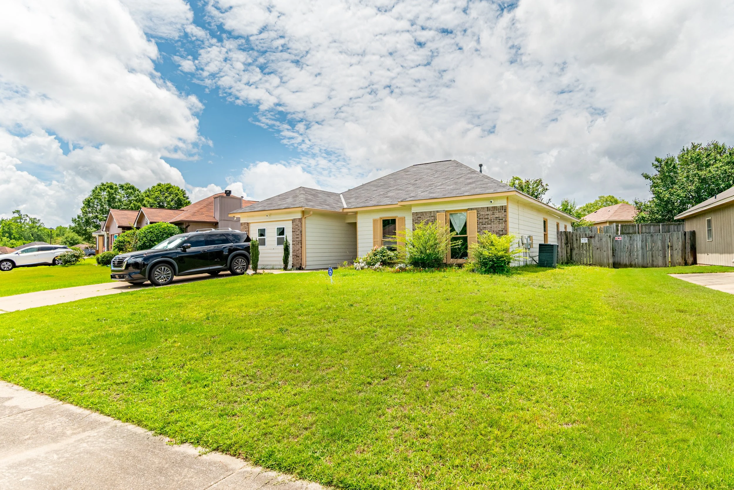 A suburban home with a neatly maintained lawn, parked cars in the driveway, and a partly cloudy sky overhead.
