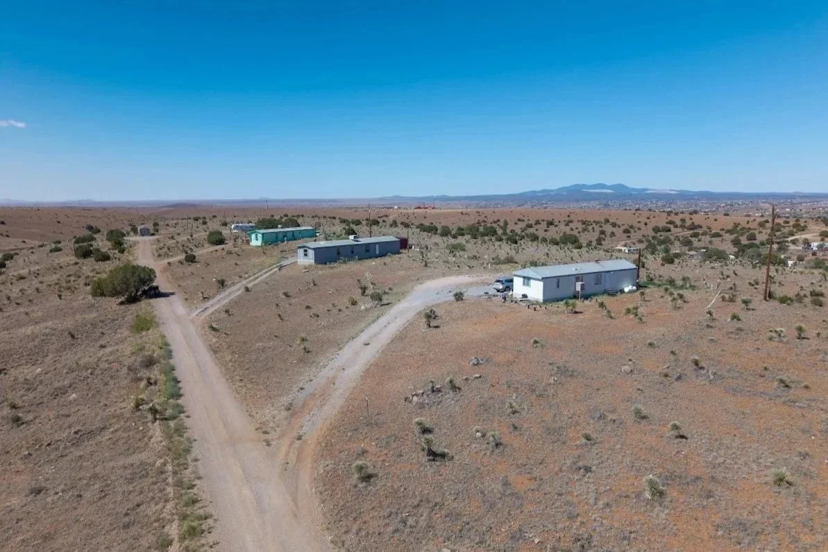 Aerial view of a sparsely populated desert landscape with a few mobile homes and dirt roads.